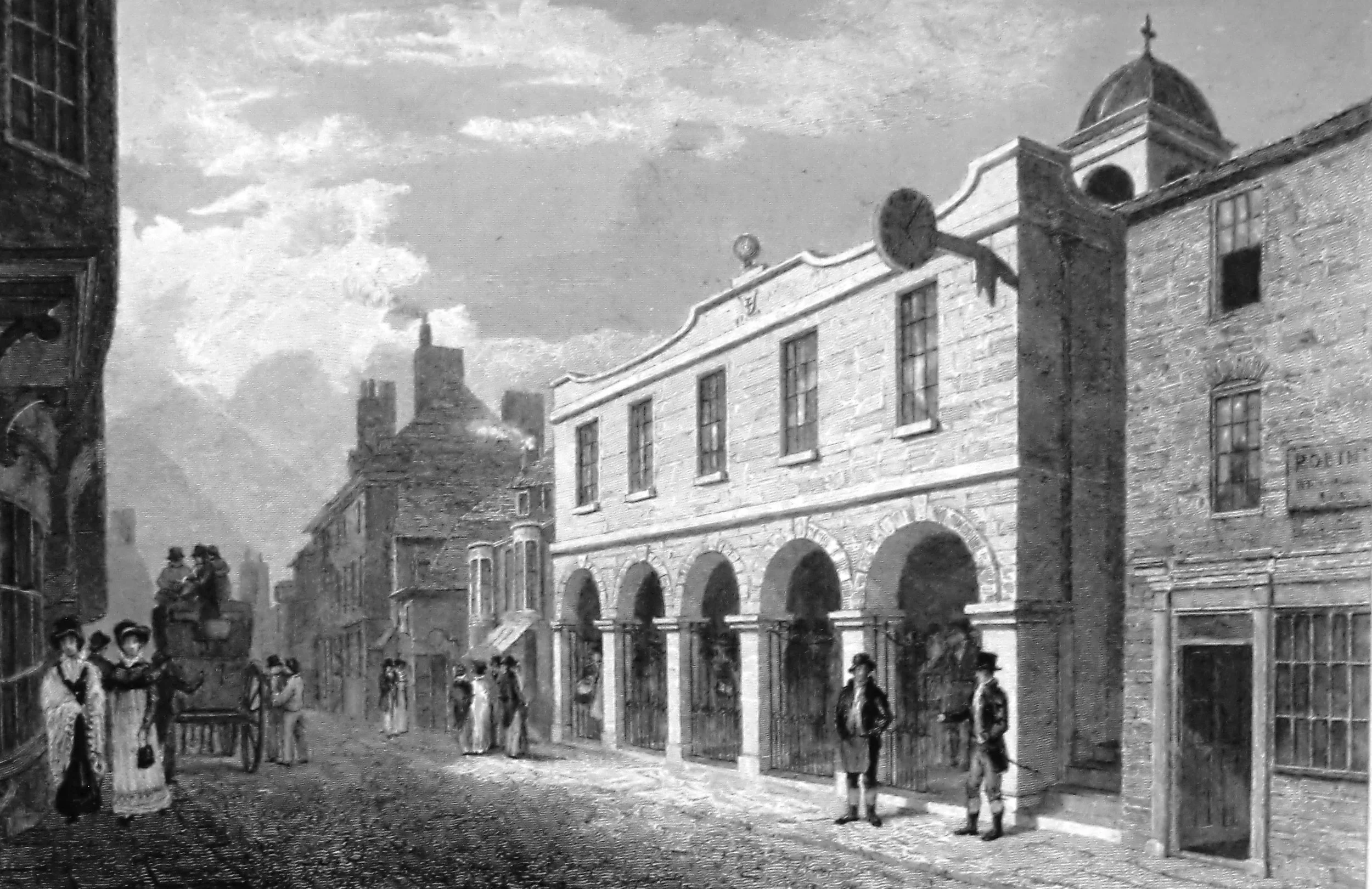 Black and white photo of a historic street scene with a large building featuring arched windows and a tower with a dome in the background. Several people are walking or standing on the street, dressed in early 20th-century clothing.