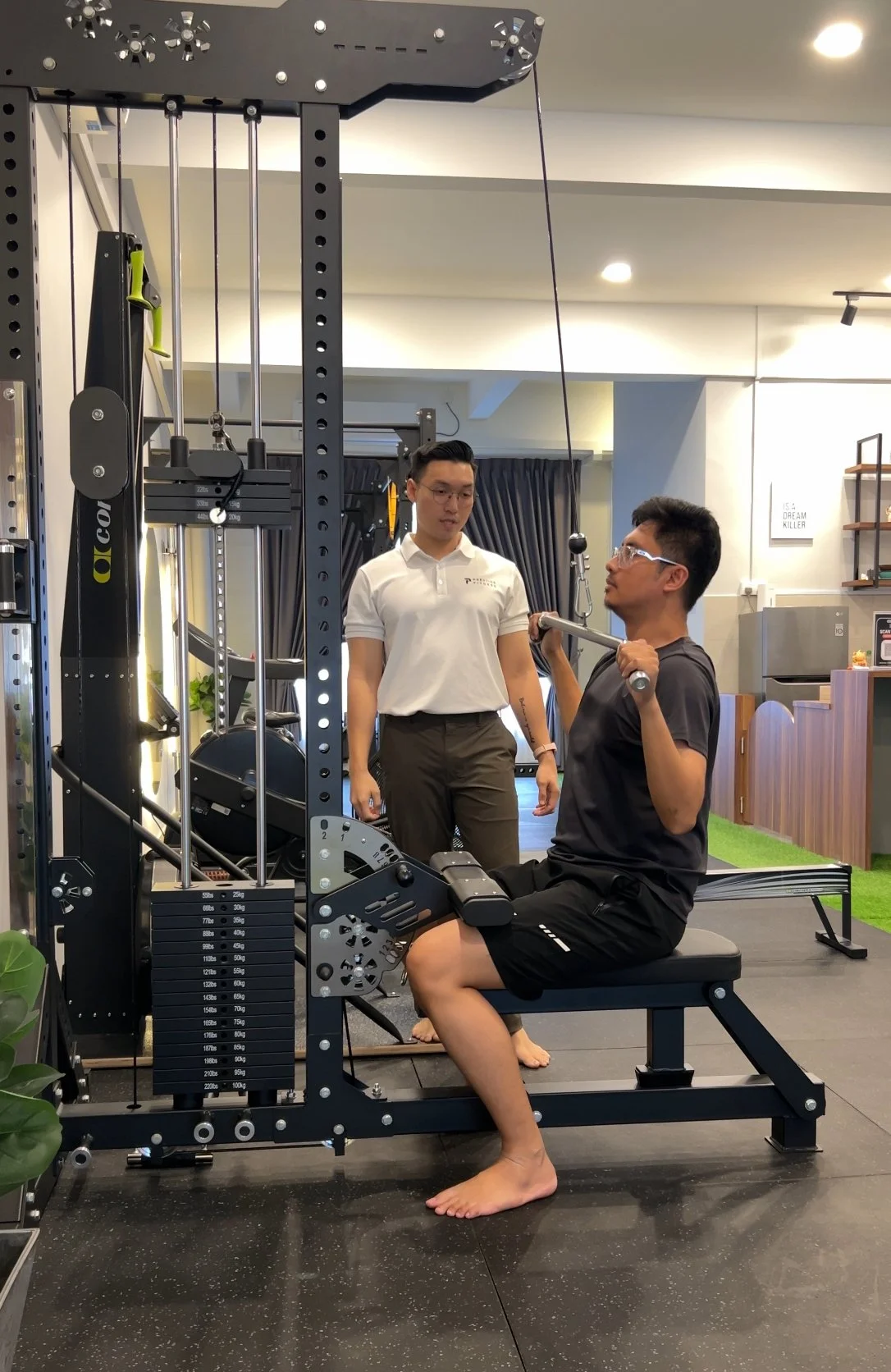 An expert personal trainer in Ipoh is coaching a successful business owner to perform pull down at Prestige Fitness Personal Training, best personal training gym in Ipoh