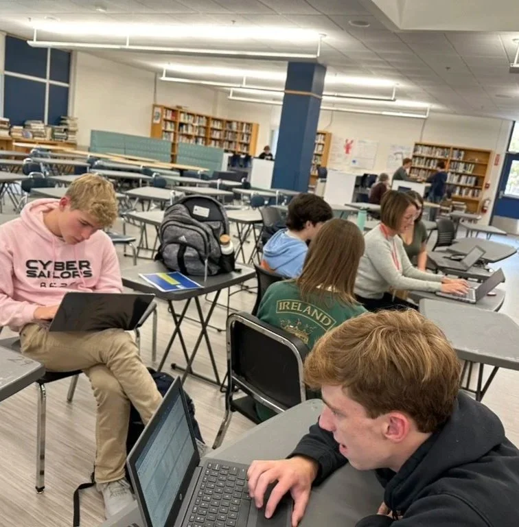 Students working on laptops in a school library or study area.