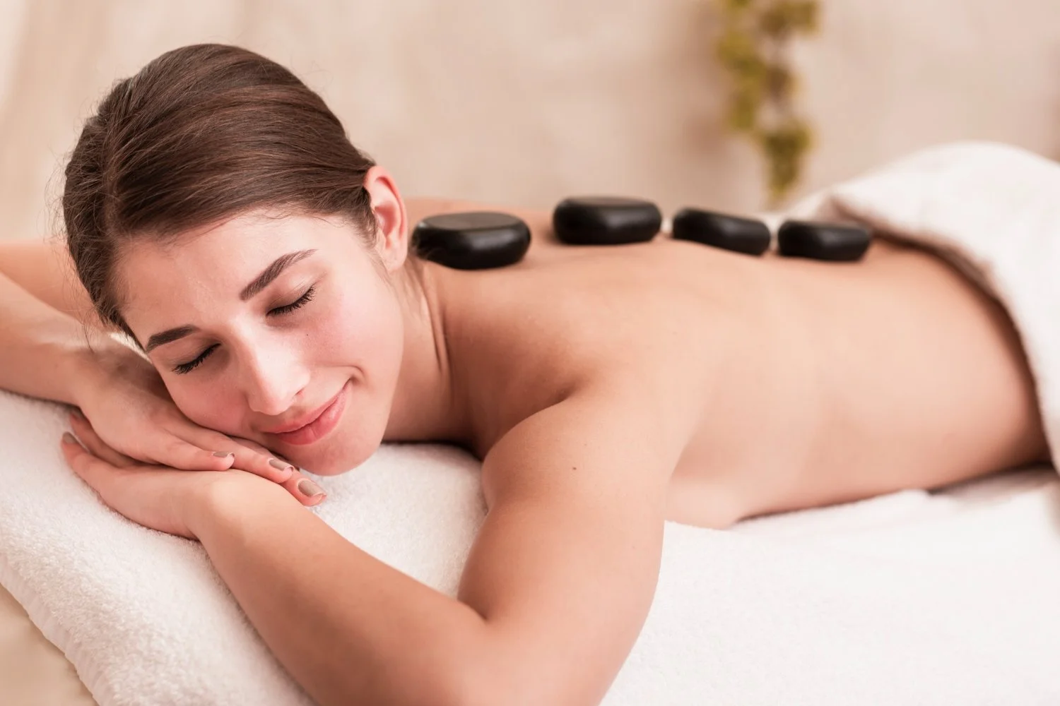 A woman receiving a hot stone massage with four hot stones placed along her back as she lies on her stomach with eyes closed.