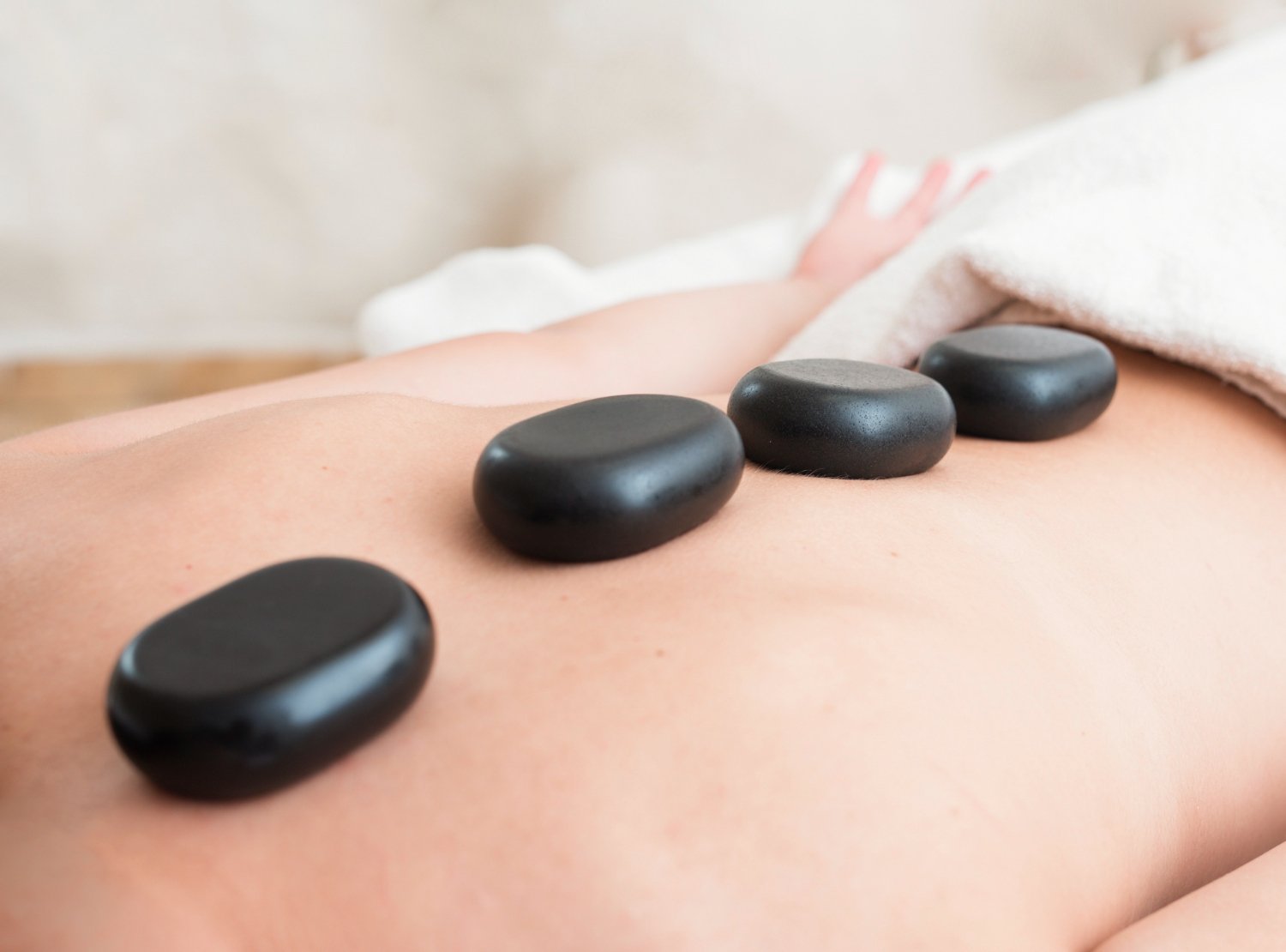 A person receiving hot stone massage therapy with five smooth black stones placed along their back.