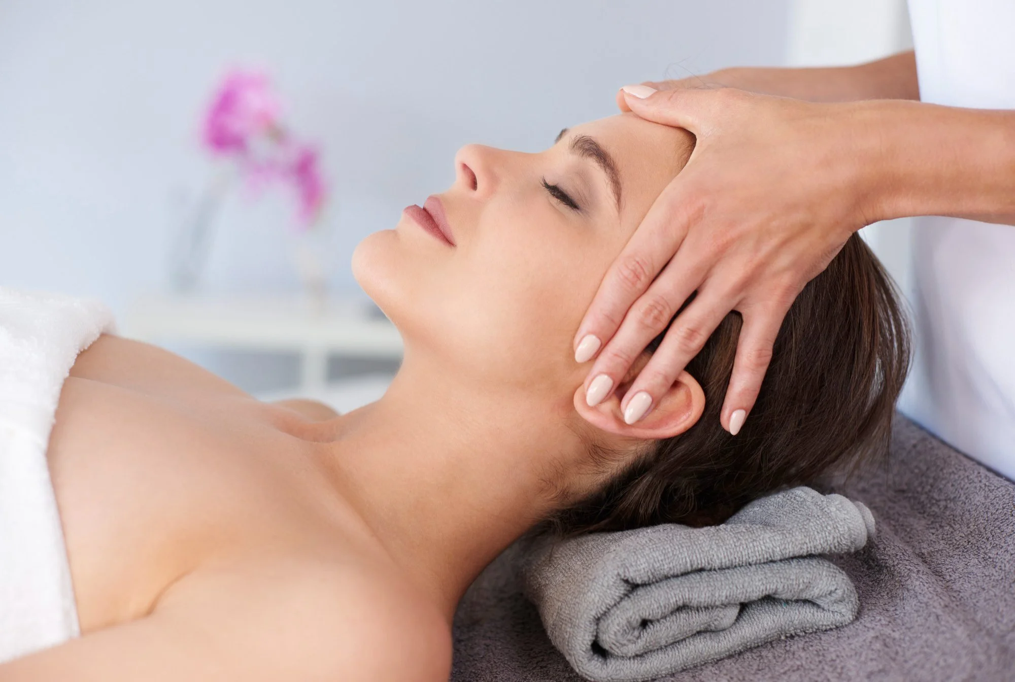 A woman receives a facial massage or treatment while lying on a spa bed.