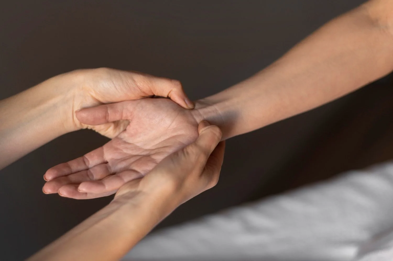 Two people are holding hands, one with a lighter skin tone and the other with a darker skin tone, against a dark background.