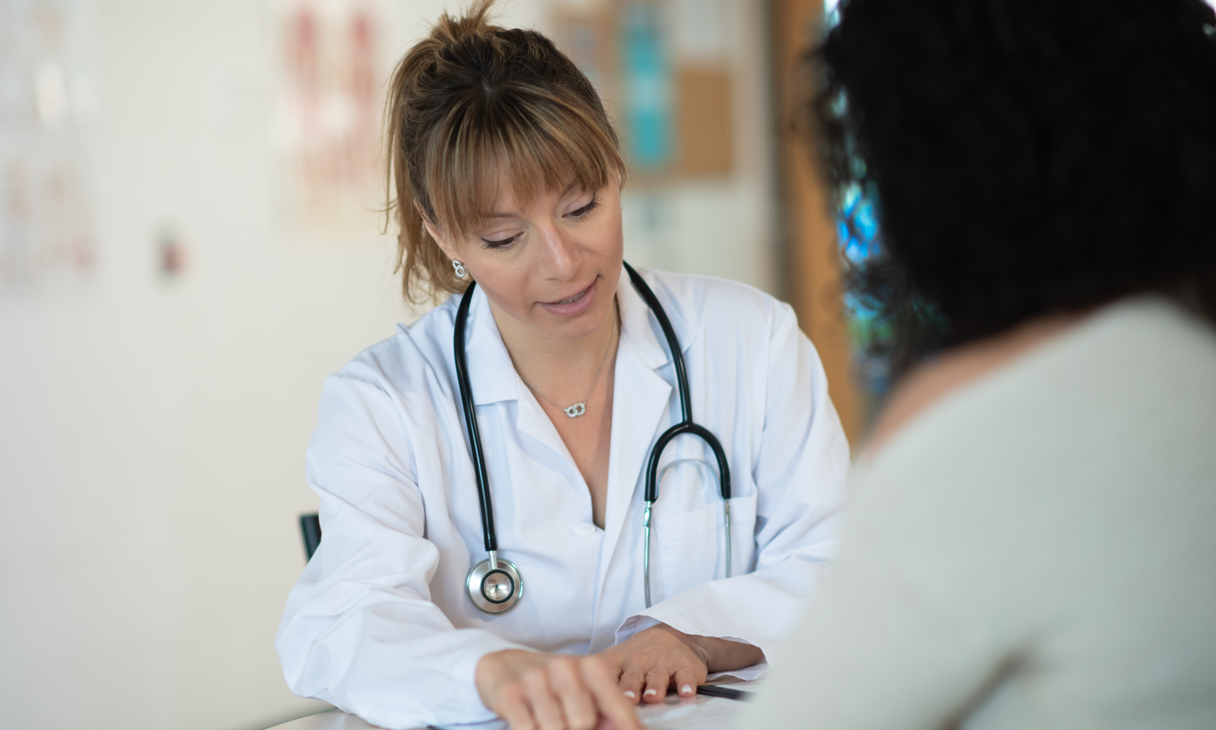 A female doctor with a stethoscope around her neck talking to a patient in a clinic.