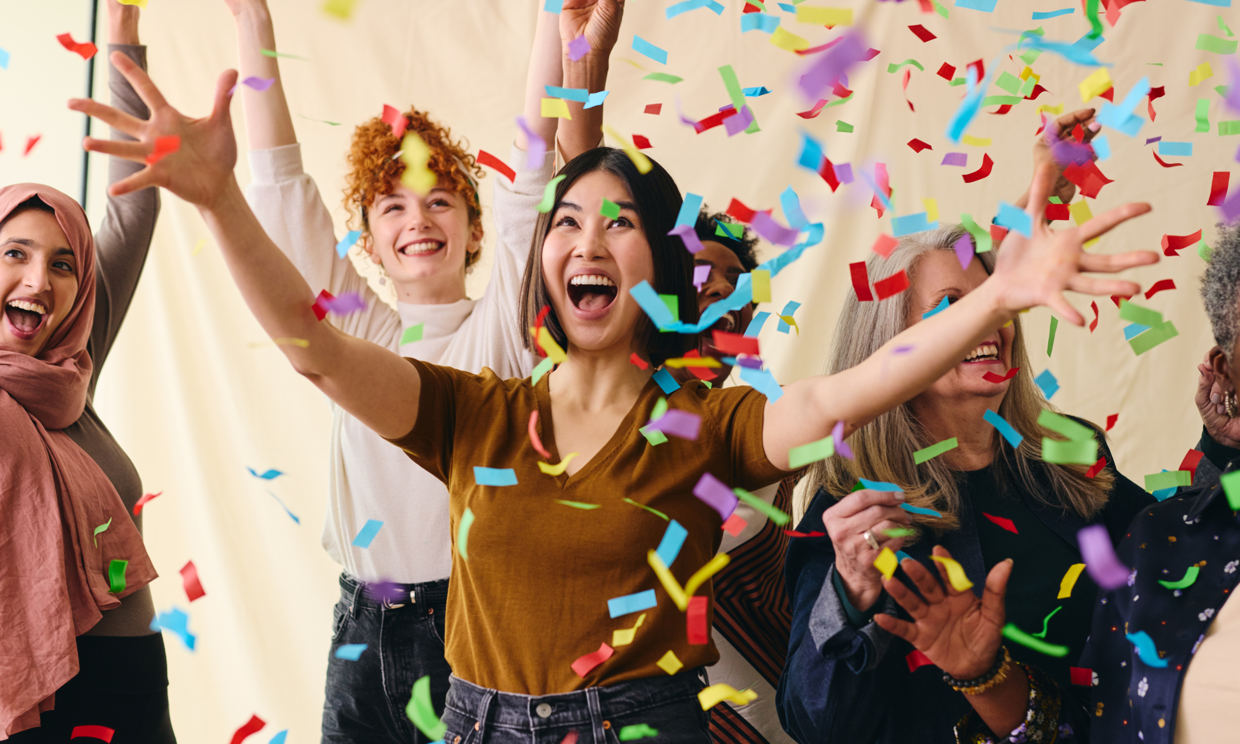 Group of diverse women celebrating with colorful confetti falling around them, smiling and enjoying a festive moment.