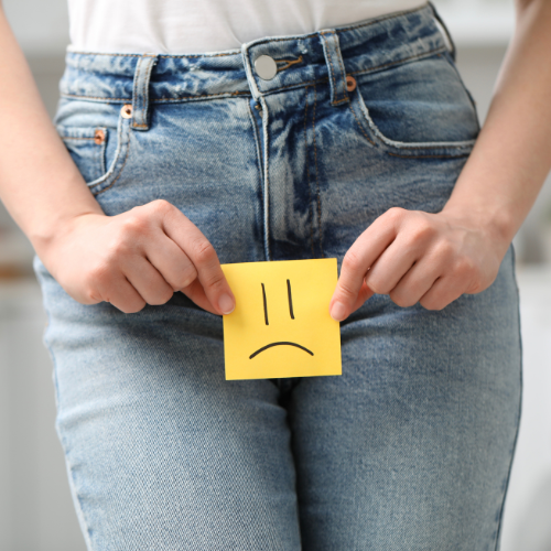 Person holding a yellow note with a sad face in front of their jeans.
