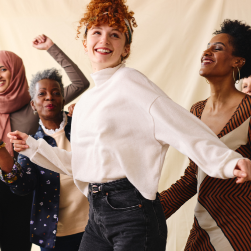 A diverse group of women dancing and smiling together indoors.