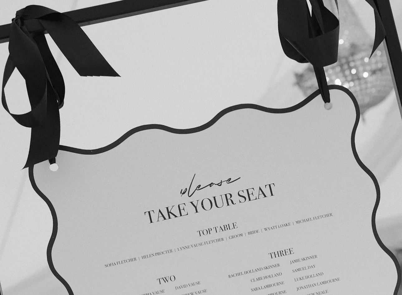 Wedding seating chart with black ribbon decorations and a white card that says 'please take your seat'.