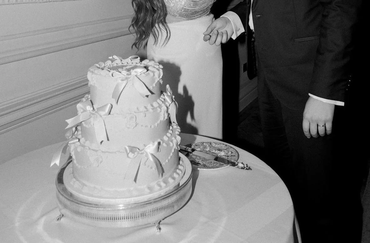 A three-tier wedding cake decorated with bows, sitting on a table during a wedding celebration.