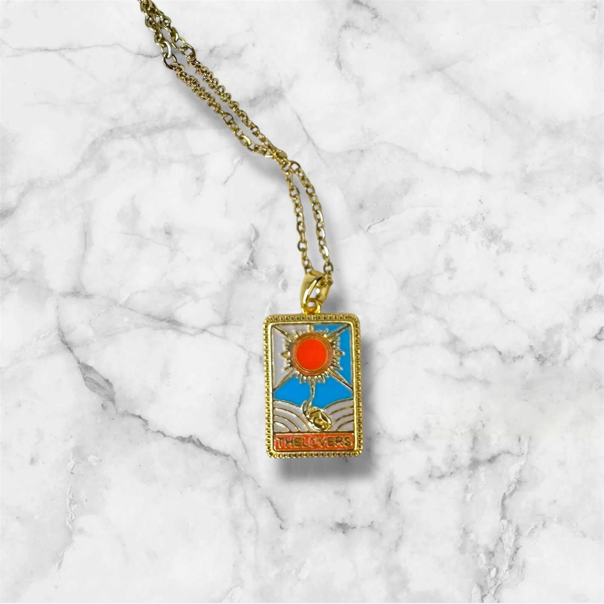 Halskette mit einem rechteckigen Anhänger, der eine Sonnen Illustration mit blauer, orange und goldener Farbe zeigt, beschriftet mit »THE LOVERS«.