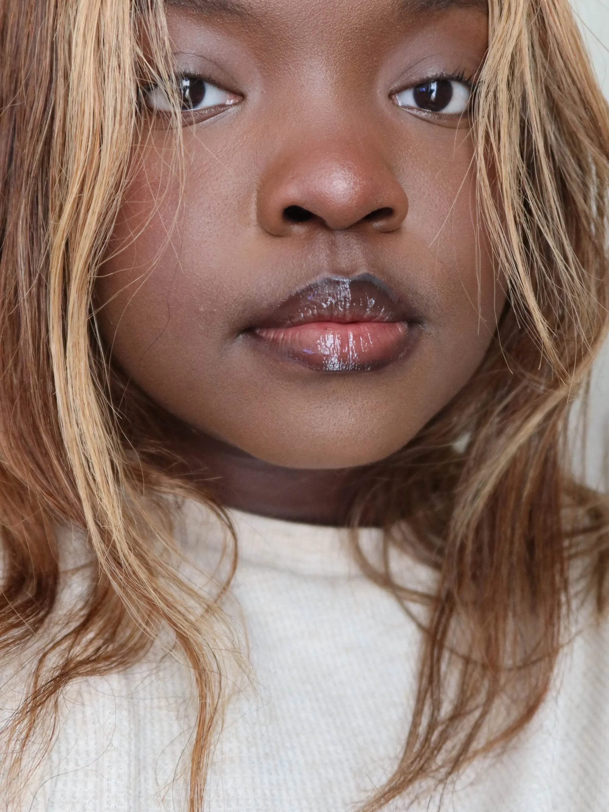 Close-up portrait of a woman with light brown skin and wavy, blonde hair, looking directly at the camera.