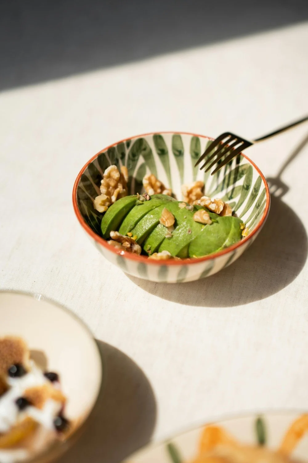 Sliced avocado with walnuts in a decorative bowl on a white tablecloth.