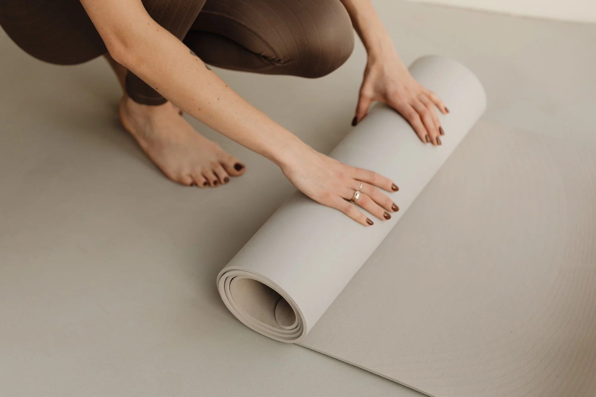Person unrolling beige yoga mat on the floor.
