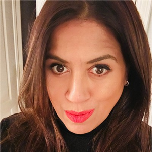 Close-up of a woman with brown hair and bright red lipstick, looking at the camera