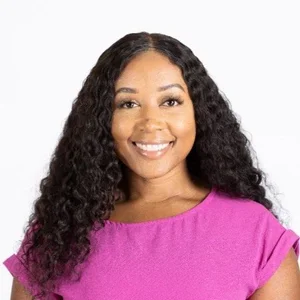 Portrait of a woman with long curly hair wearing a pink top and smiling against a white background.