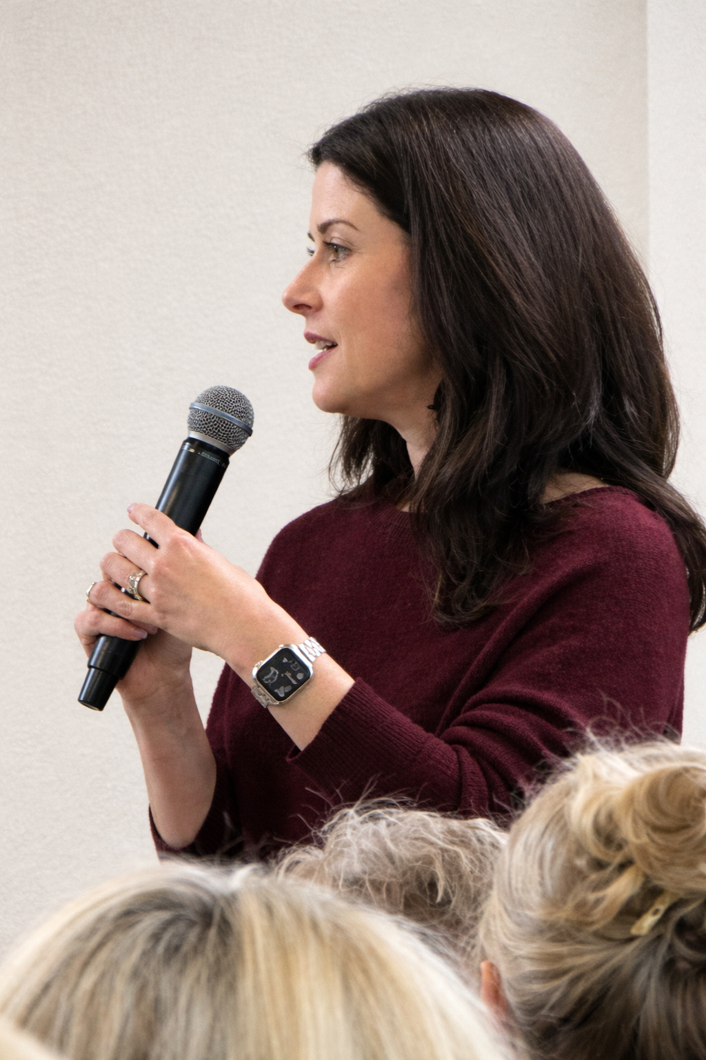 Young woman with curly hair posing with her arms raised, wearing a yellow jacket, against a plain white background.