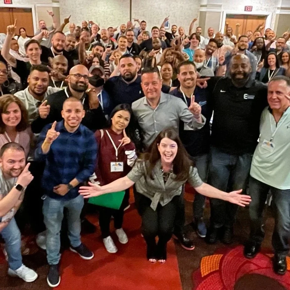 A large group of smiling people at a conference or event, posing for a group photo in a banquet room.
