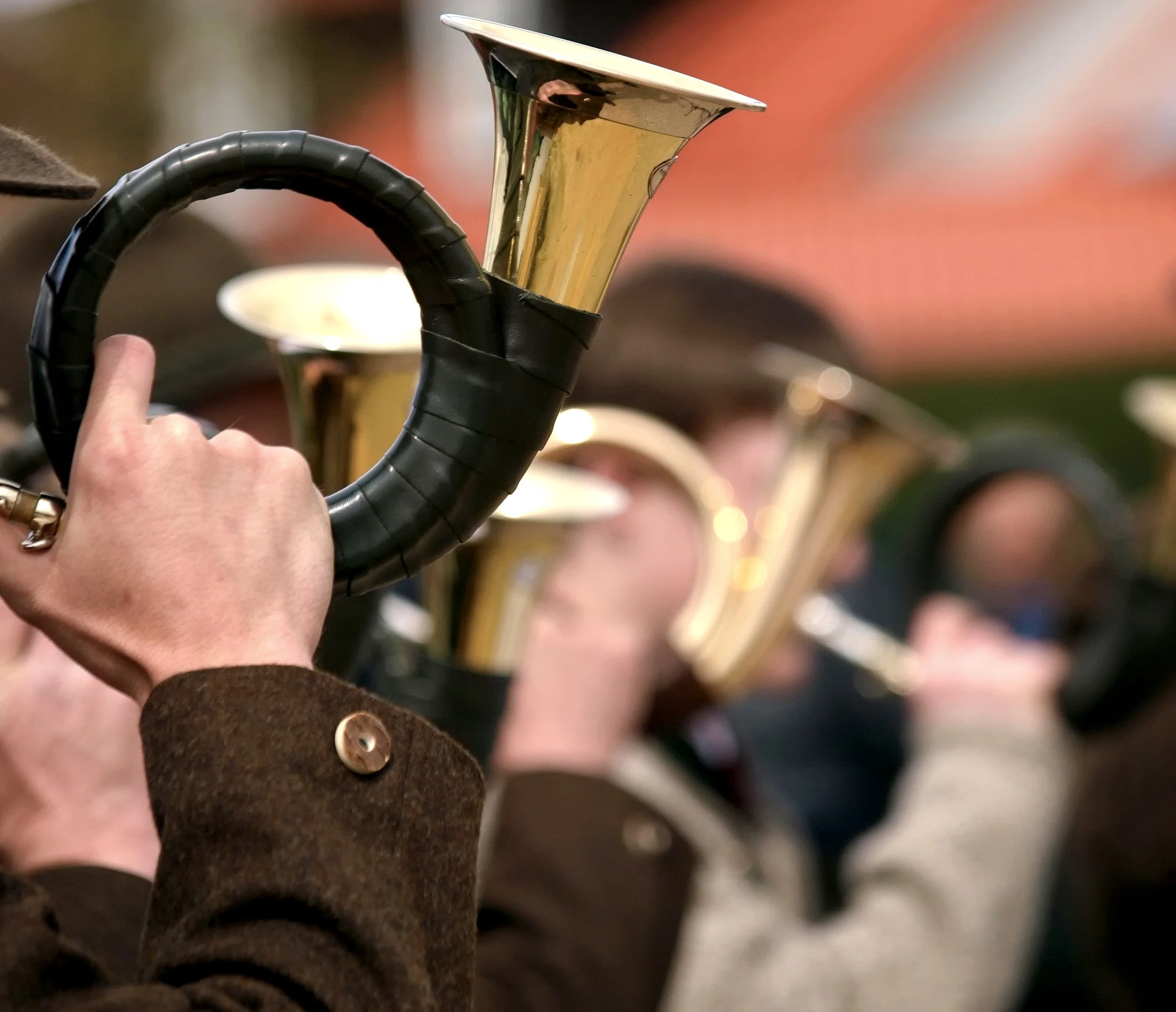 Menschen beim Musizieren mit Blasinstrumenten, im Fokus eine Person mit einem goldenen Jagdhorn.
