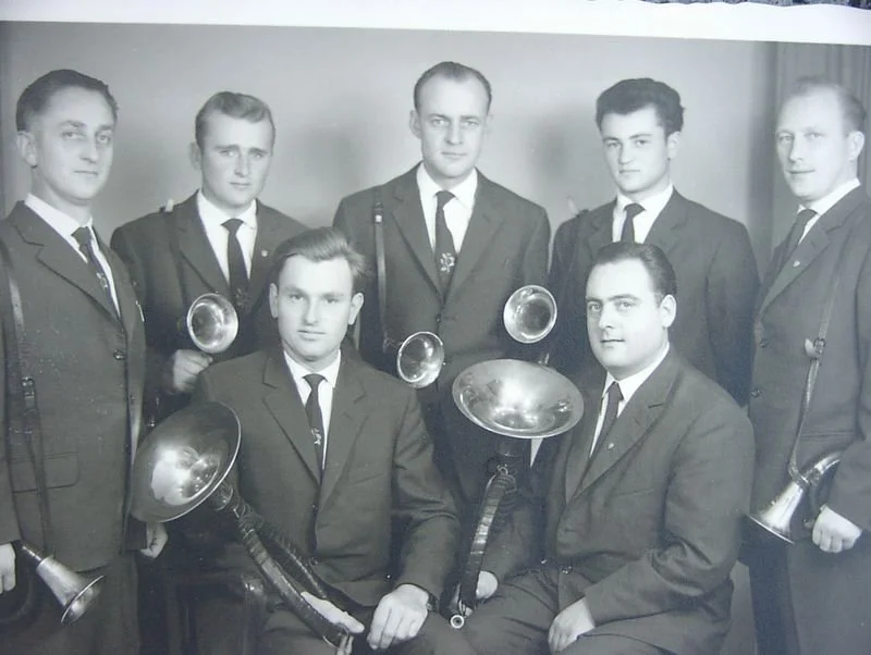 Sieben junge Männer in Anzügen, einige halten kesselförmige Musikinstrumente, in einem Schwarz-Weiß-Foto.