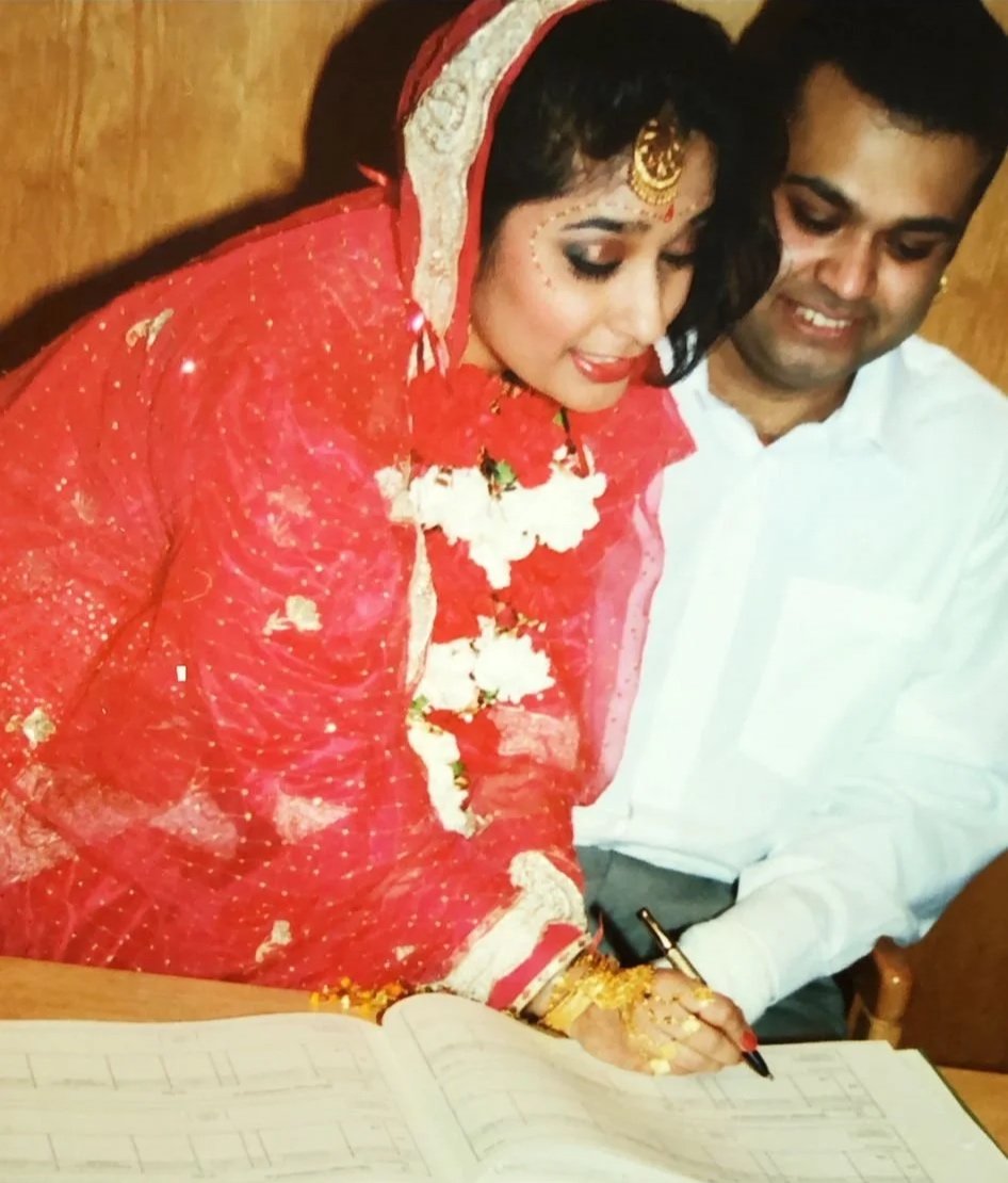 Old photo of couple on their wedding day signing registry book with bride in traditional indian red and groom in white shirt