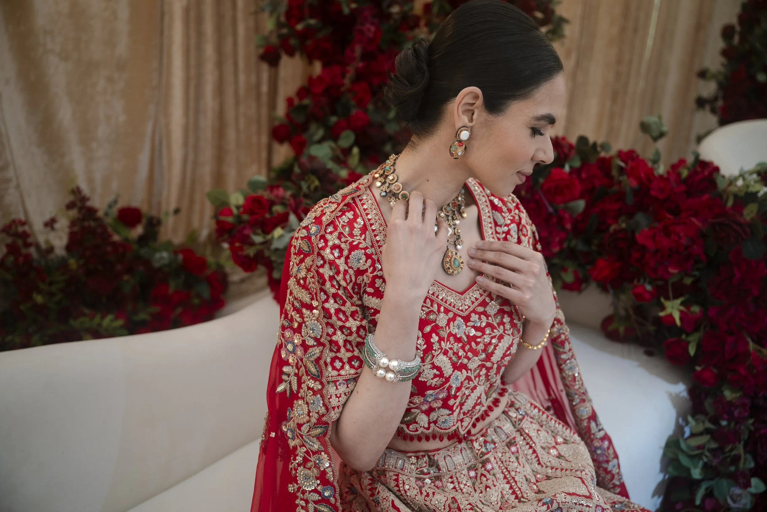 Indian bride in red sherni London lehenga looking away touching jewellery