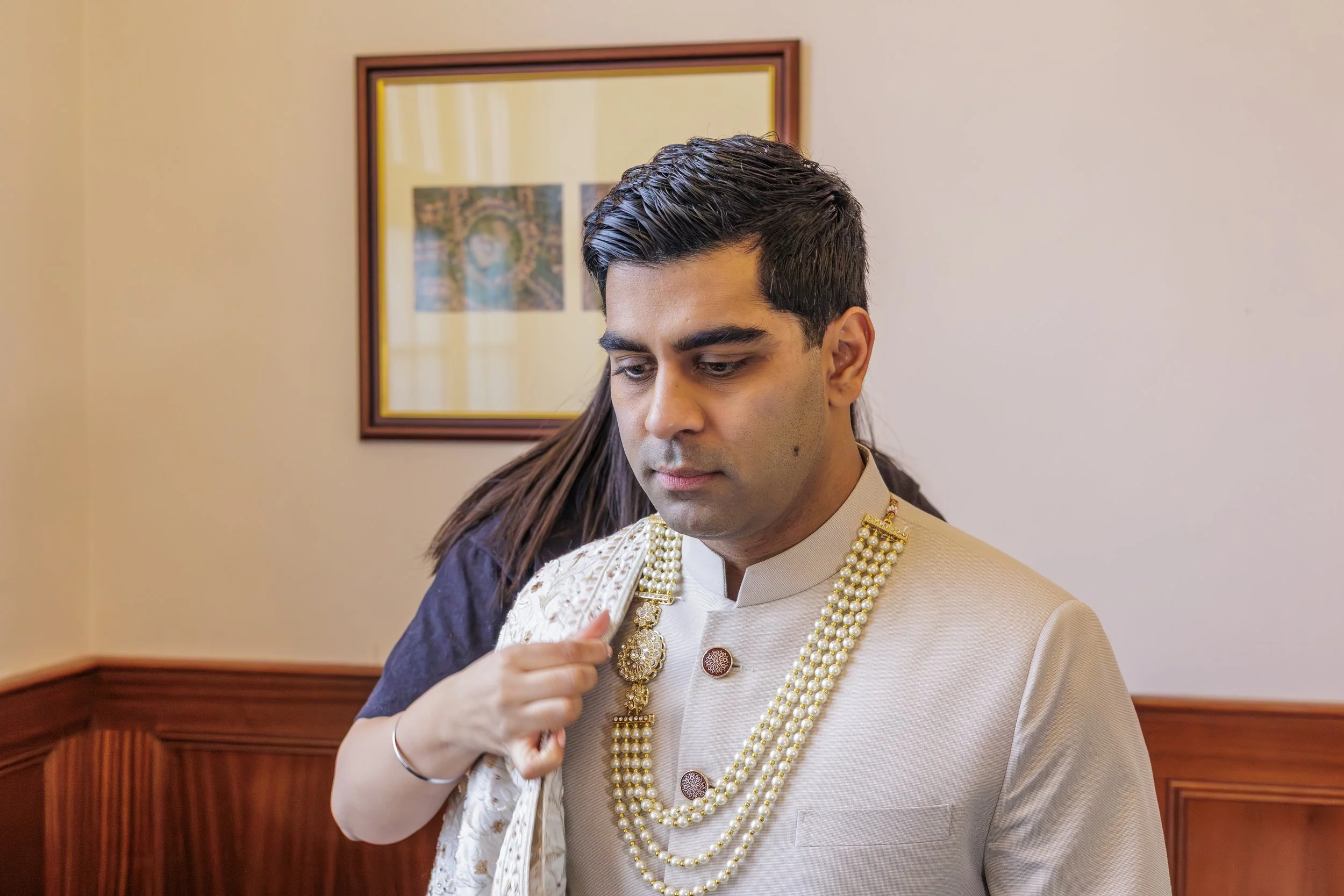 Menswear supplier getting groom ready wearing beige sherwani draping his palla shawl and fixing his outfit