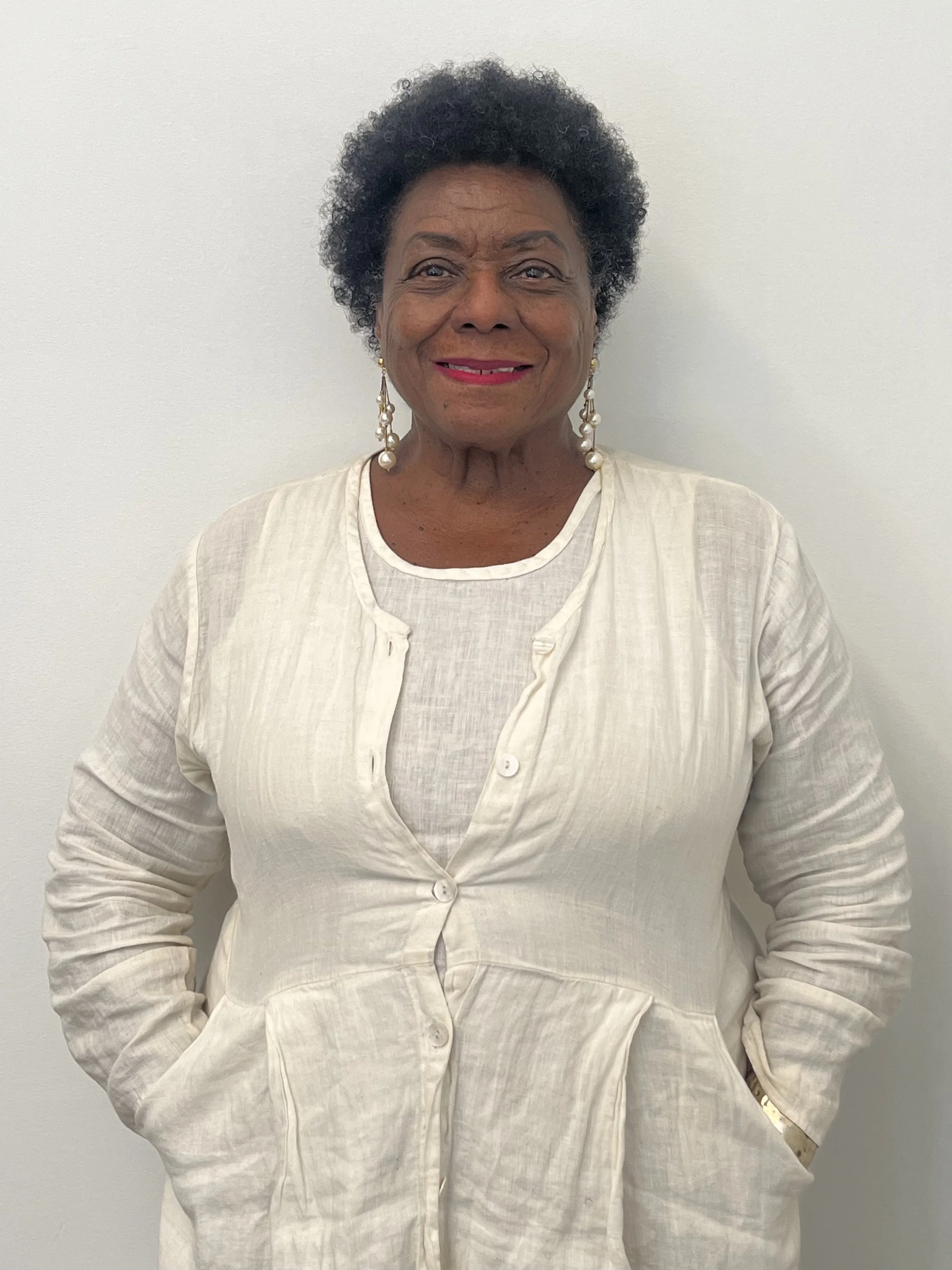 Veronica Jones, an older Black woman with shot hair, in front of a blank wall wearing a monochromatic white outfit