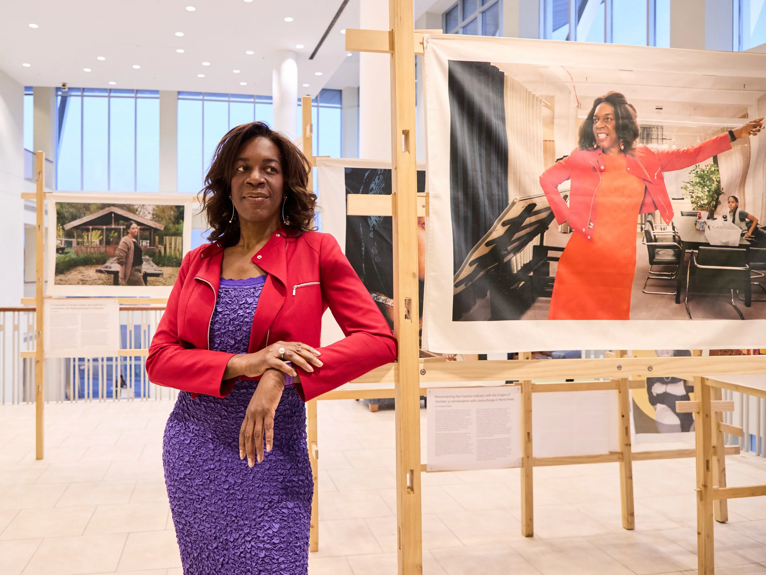 Ngozi Okaro in a purple dress and red jacket poses next to a display photo of her in the Museum of Fashion and Liberation exhibit in Boston 