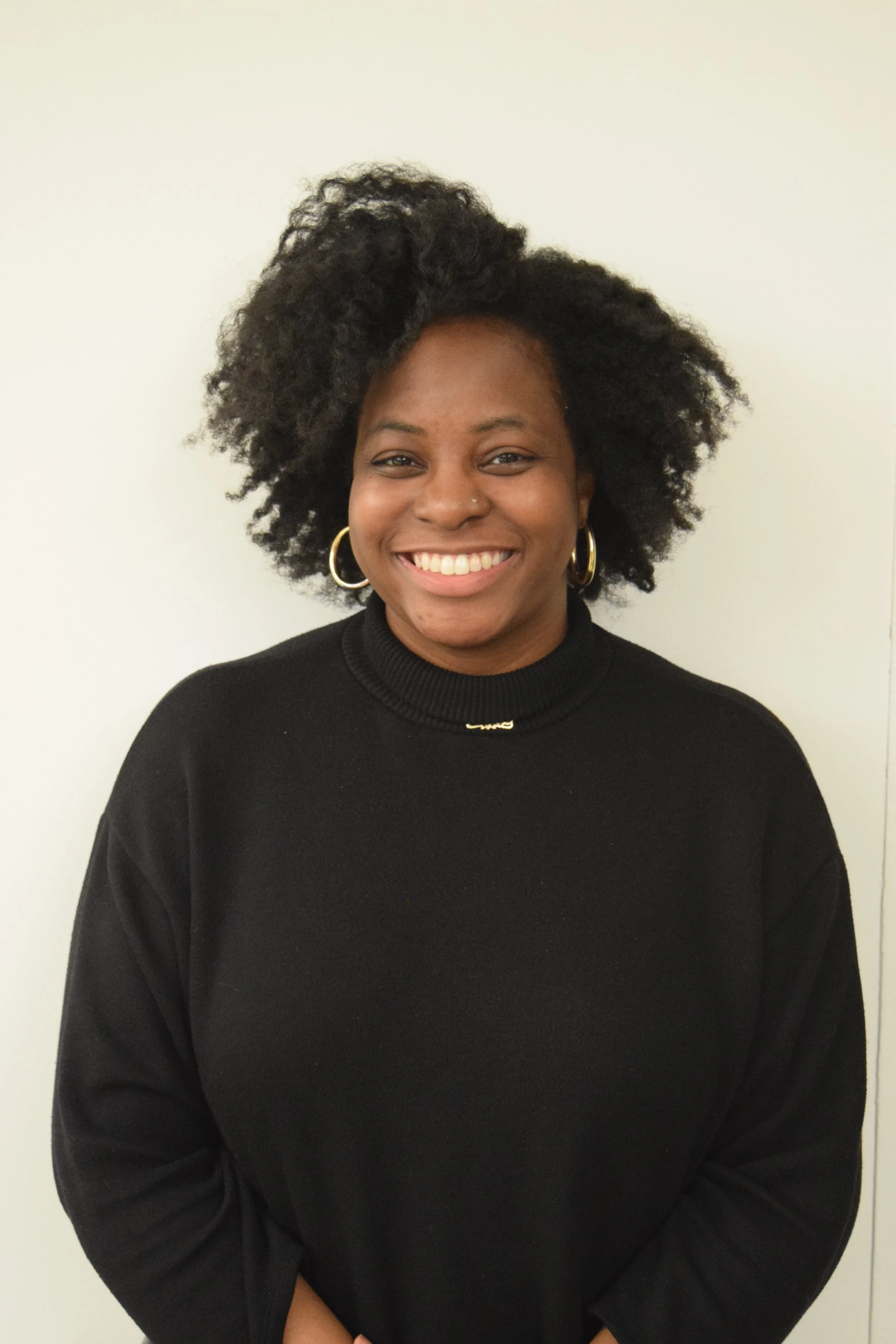 A Black woman with full curly hair wearing gold hoop earrings and a black sweater