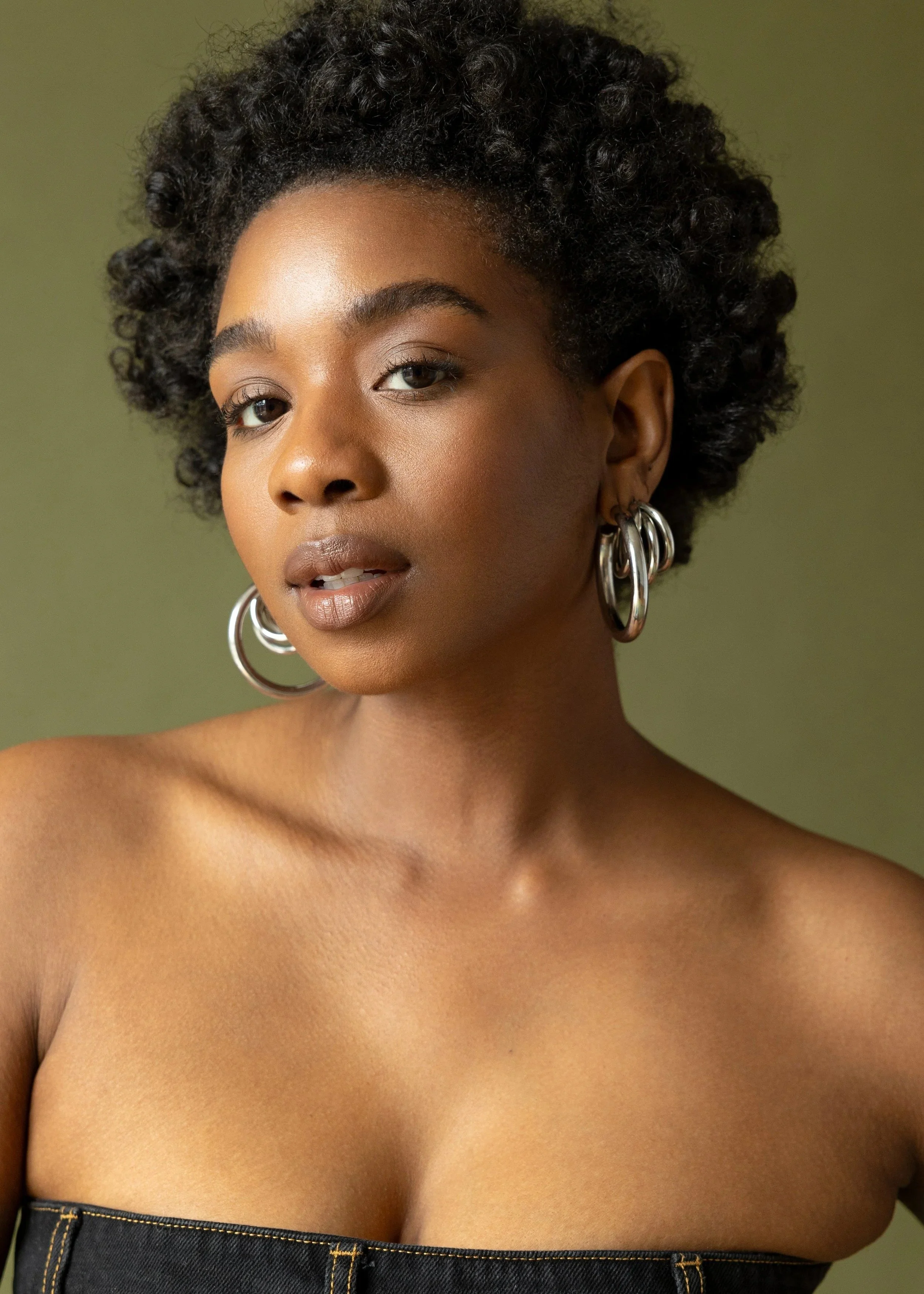 A Black woman with short hair wearing large silver hoop earrings and a strapless top