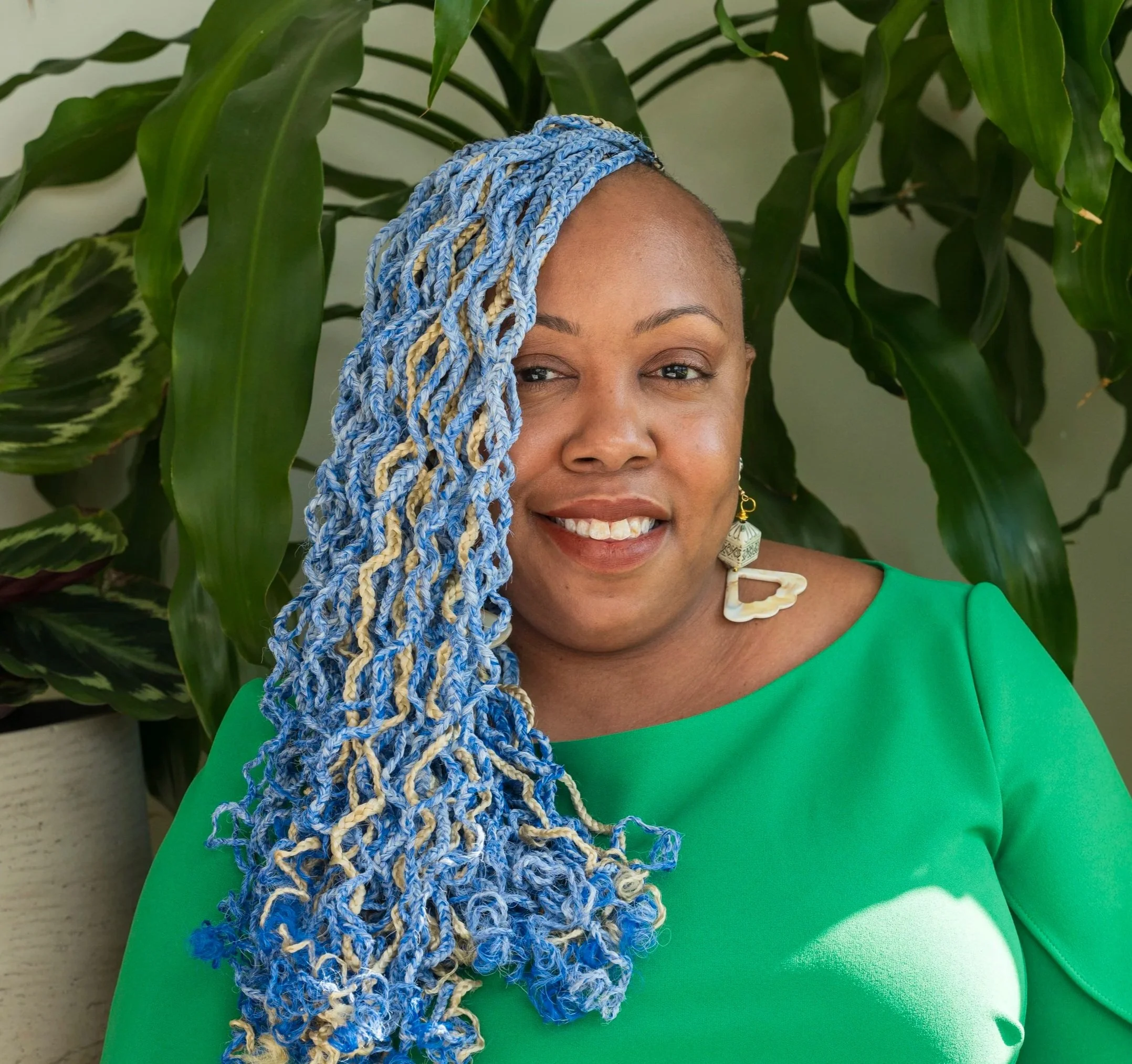 A woman smiling, she was blue and blonde wavy braids and a green top