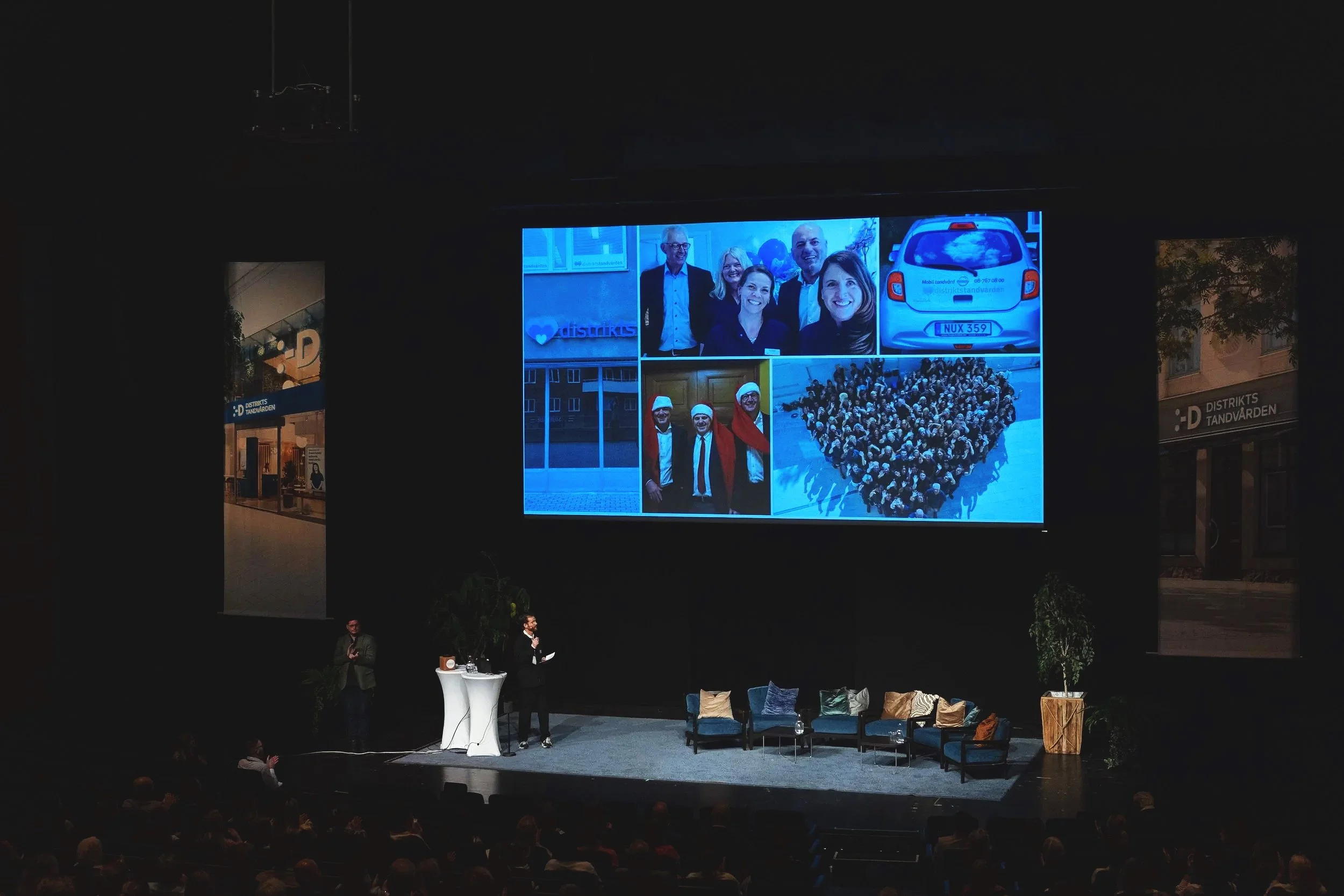 A large screen displays collage of images at a presentation in wisby strand. The presenter stands at a podium with a big audience in the auditorium.
