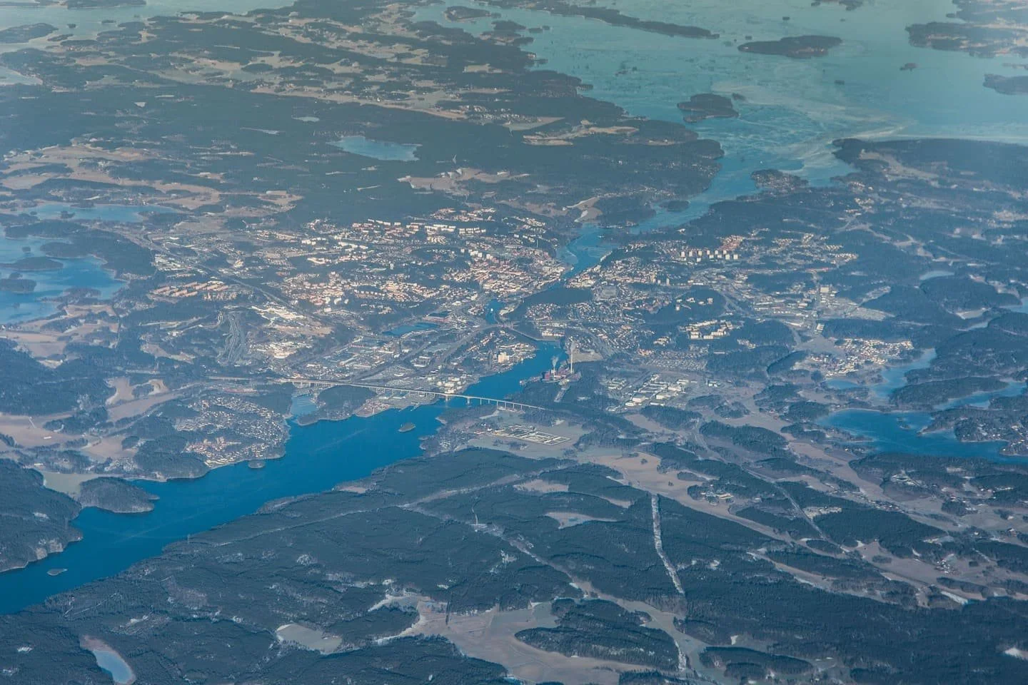 An aerial view of a city with a river running through it, surrounded by forests and open land. Södertälje