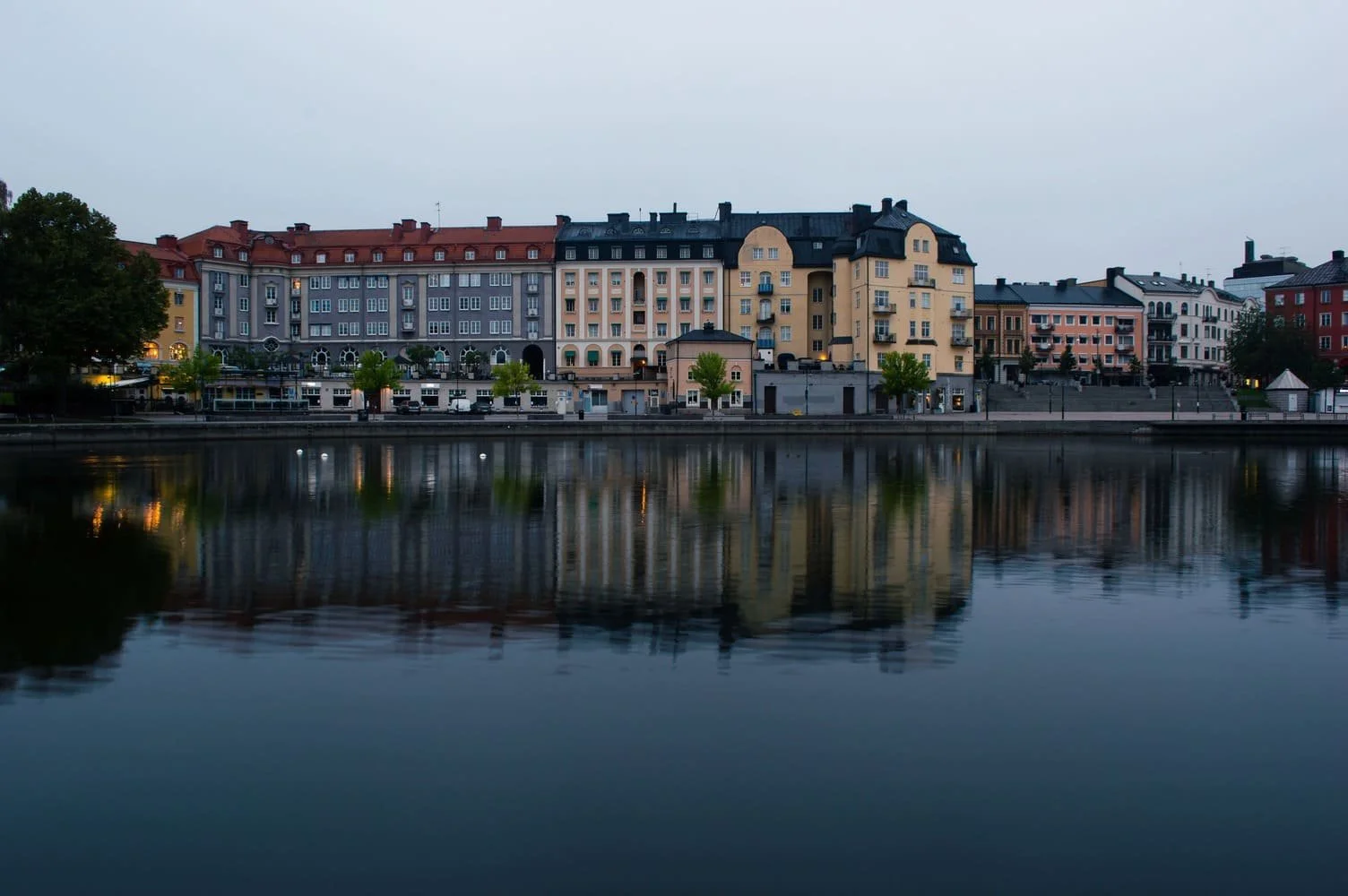 Colorful buildings along a waterway with their reflections visible in the water at dusk. Södertälje