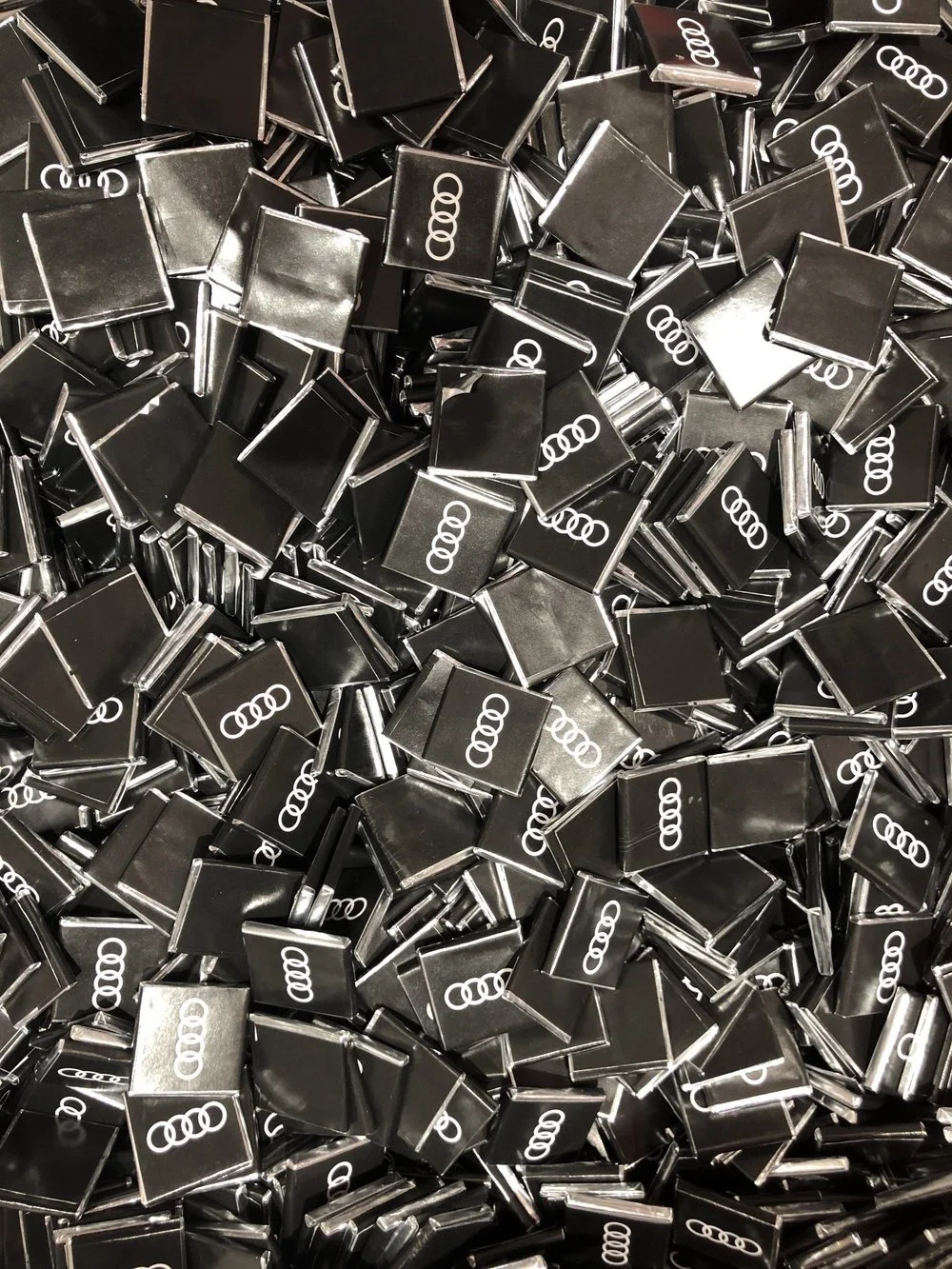 A large pile of black square pins with the Audi logo printed in white.