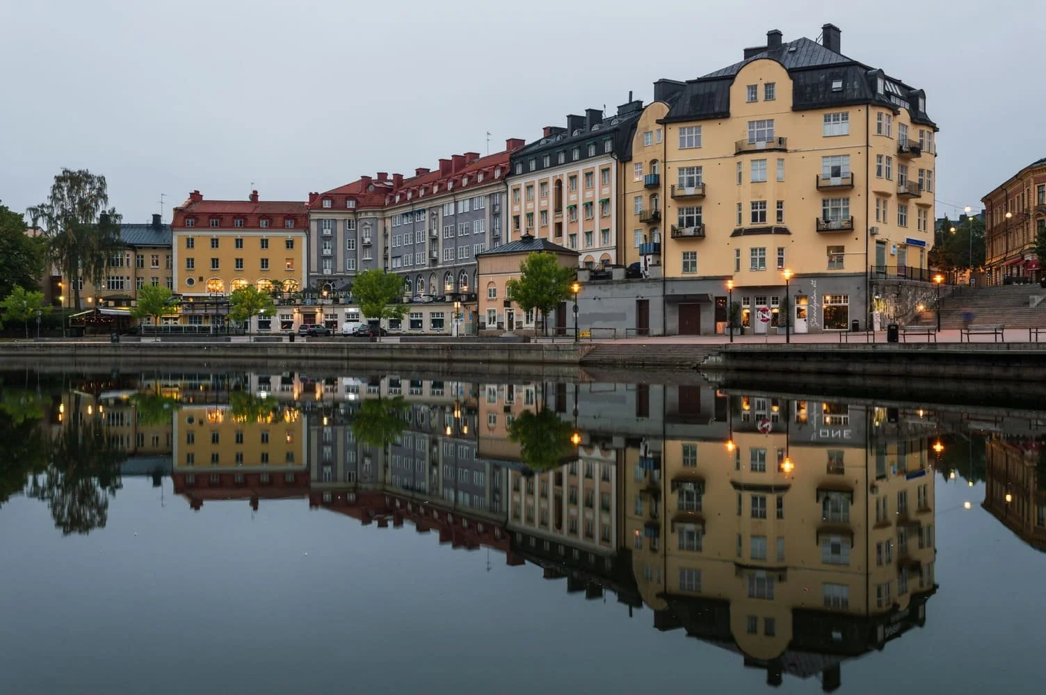Colorful European-style buildings along a waterway at dusk with their reflections visible in the water. södertälje maren