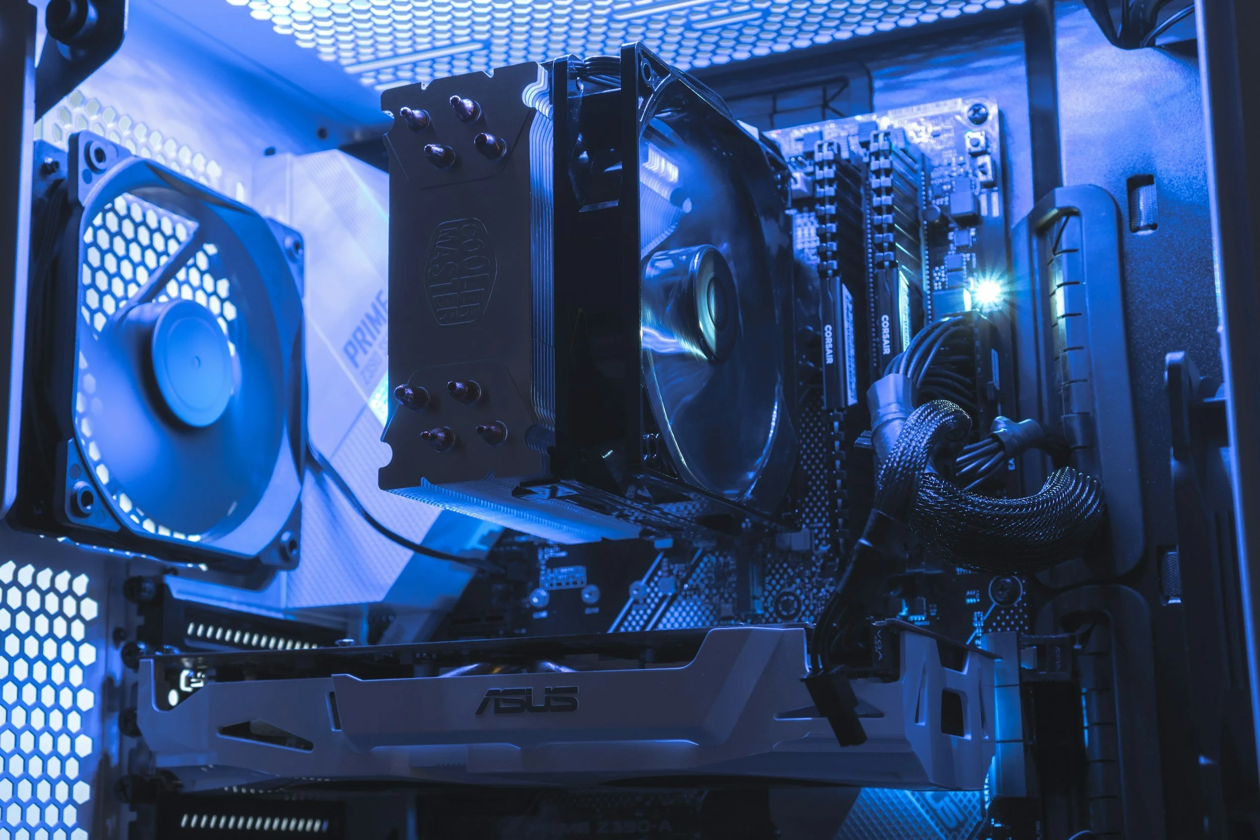 Inside a computer case showing a cooling fan, CPU cooler, RAM modules, graphics card, and power supply with blue lighting.