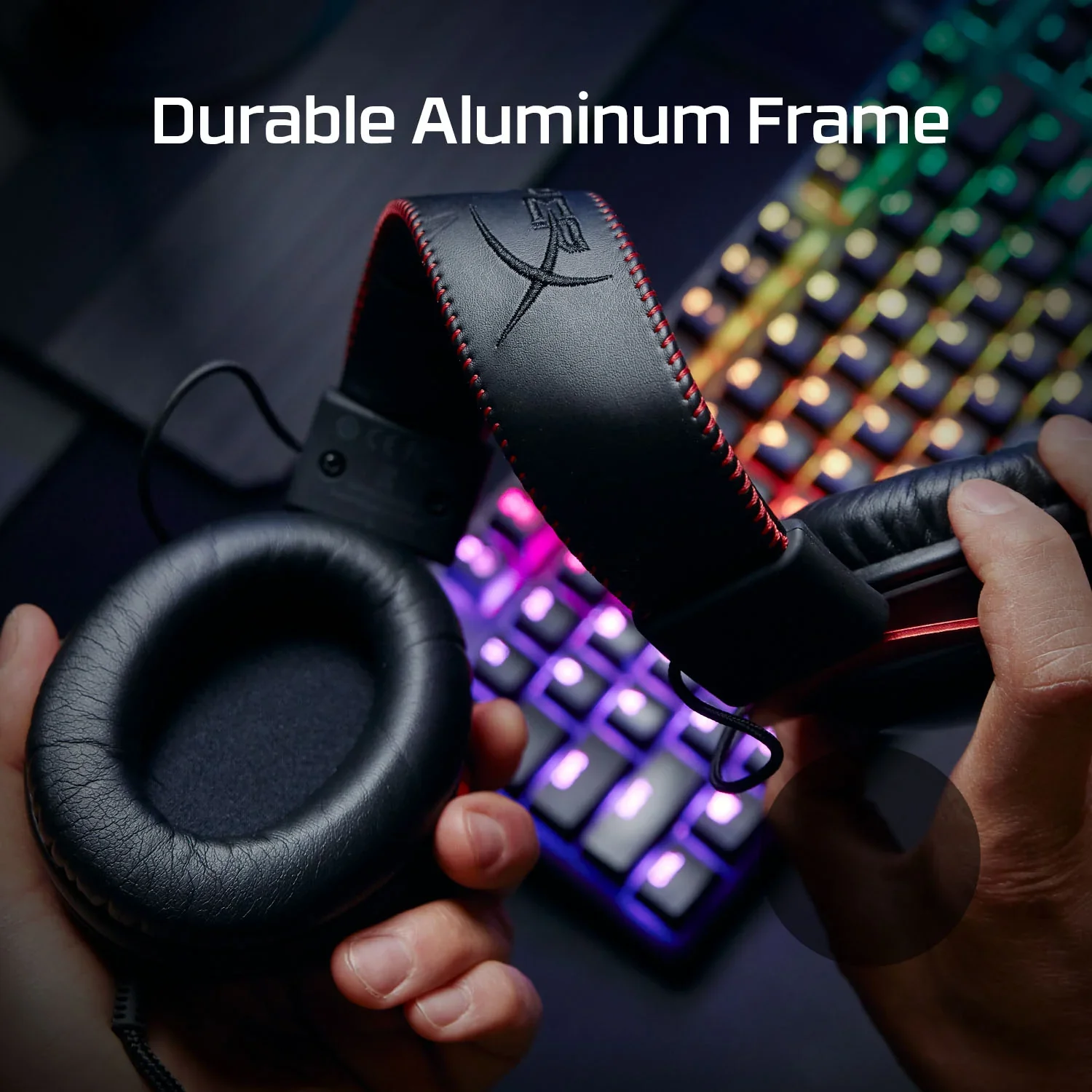 A person holding a pair of over-ear headphones with a black leather headband, stitched with red thread, and black padded ear cups. The headphones are placed above a colorful illuminated keyboard with rainbow-colored backlit keys, and the image has the caption 'Durable Aluminum Frame' at the top.