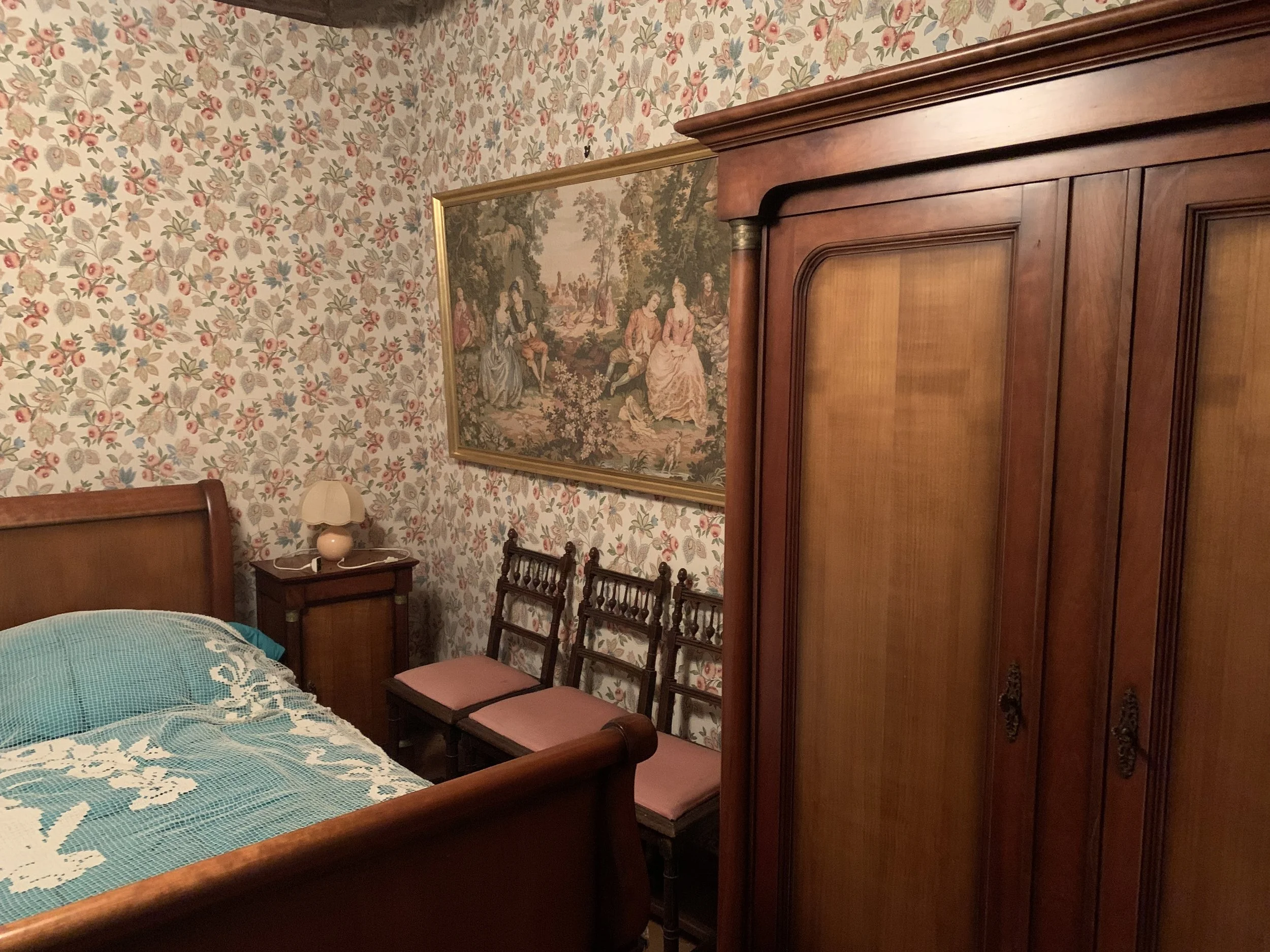 Avant la transformation en cuisine - Chambre avec un lit en bois, une armoire, un tableau de style classique, murs recouverts de papier peint à motifs floraux.