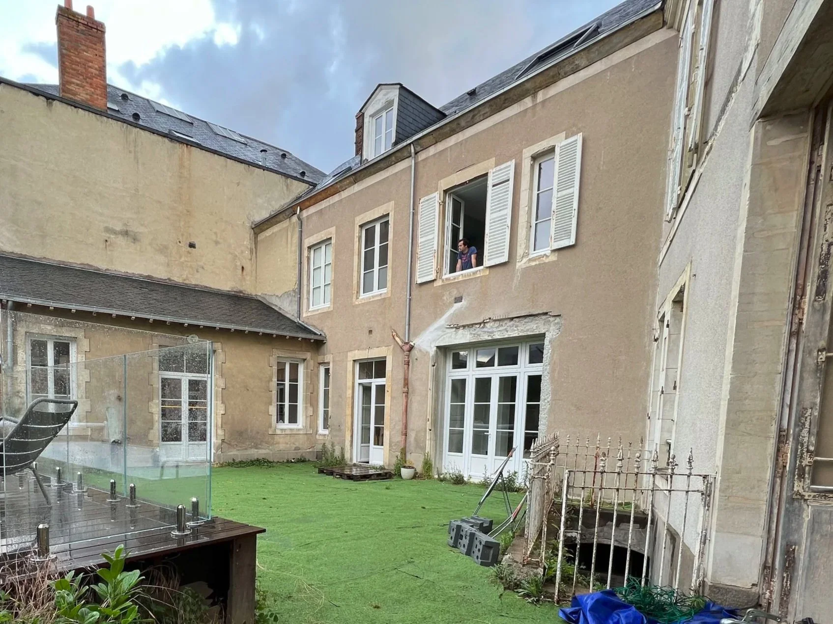 Cour arrière d'une maison avec des murs défraîchis, des fenêtres,  et un ciel nuageux avant la rénovation.