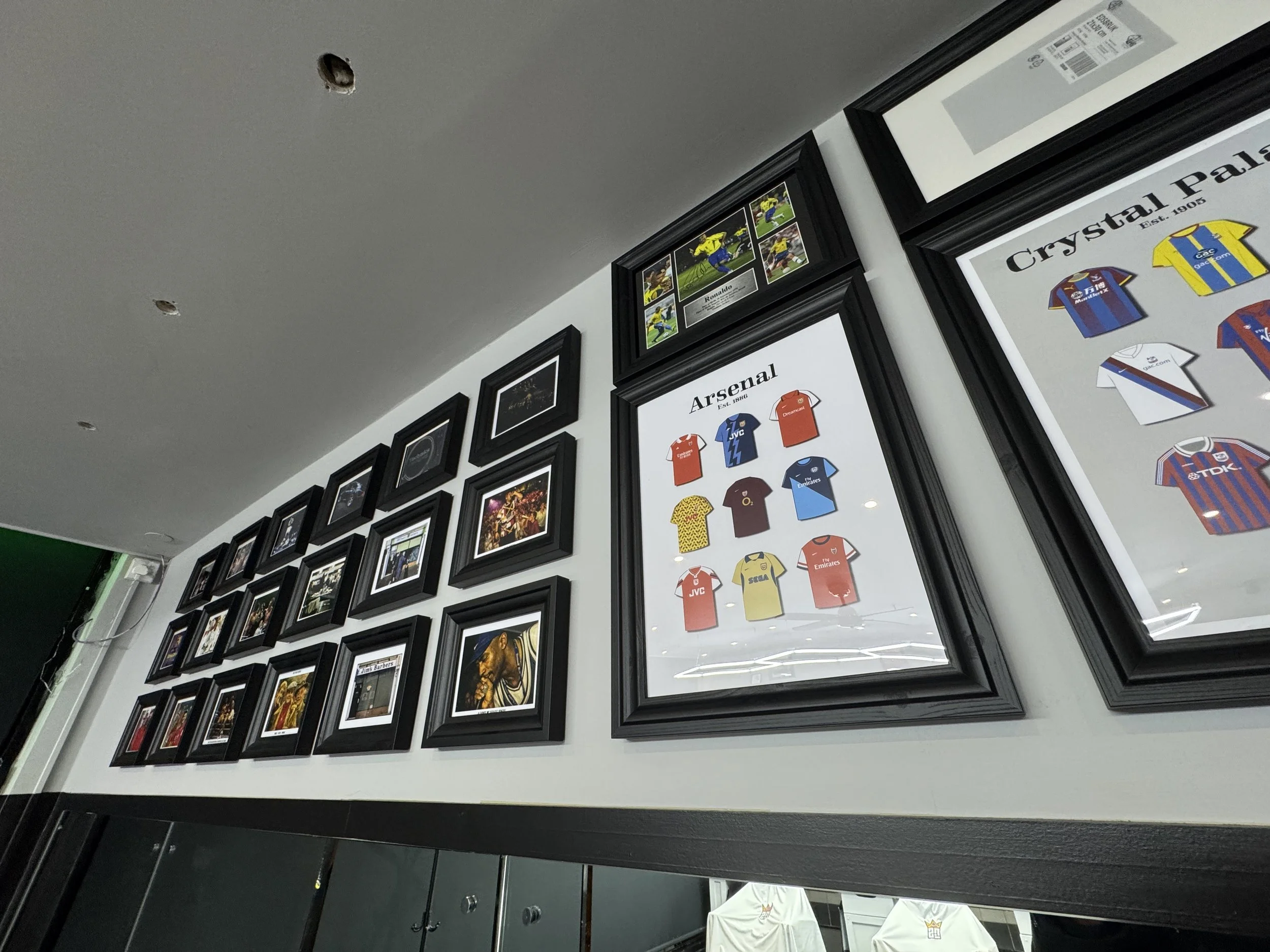 Wall display of framed sports memorabilia, including jerseys of Arsenal and other soccer teams, with photographs and posters.