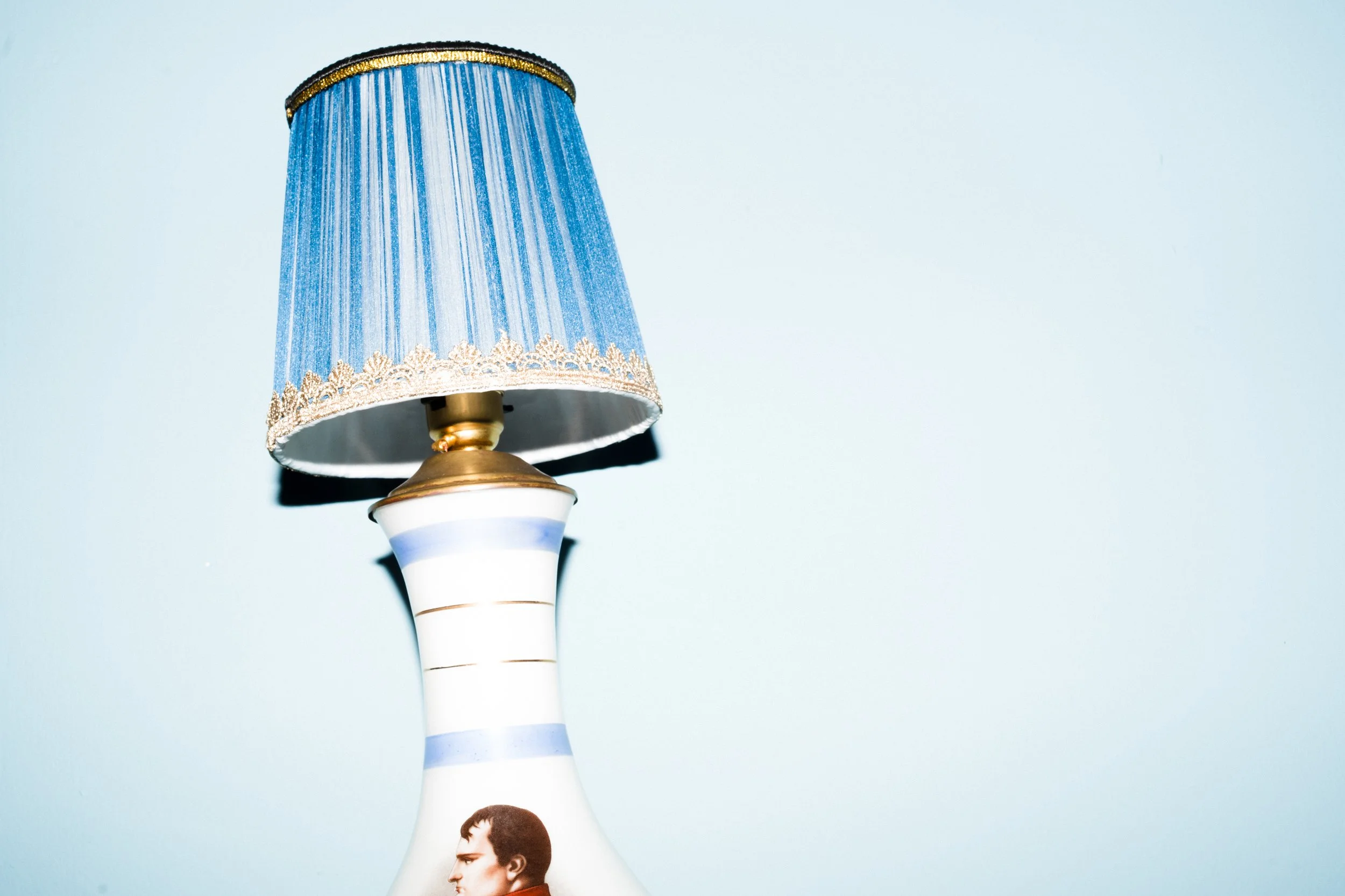 Close-up of a decorative table lamp with a blue lampshade and a ceramic base featuring a young man's profile.