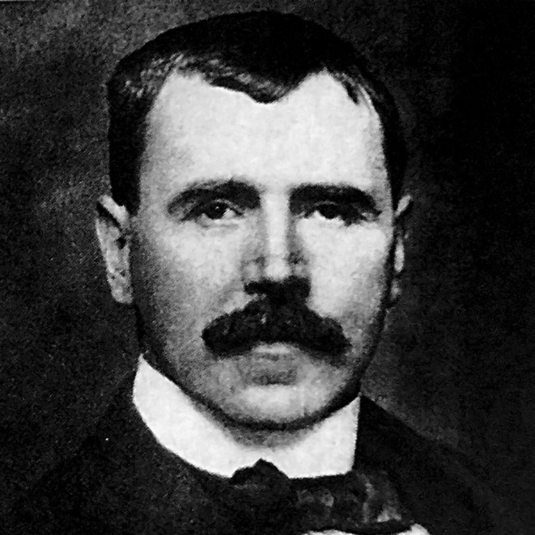 Black and white portrait of a man with dark hair, a mustache, and formal clothing, including a bow tie.