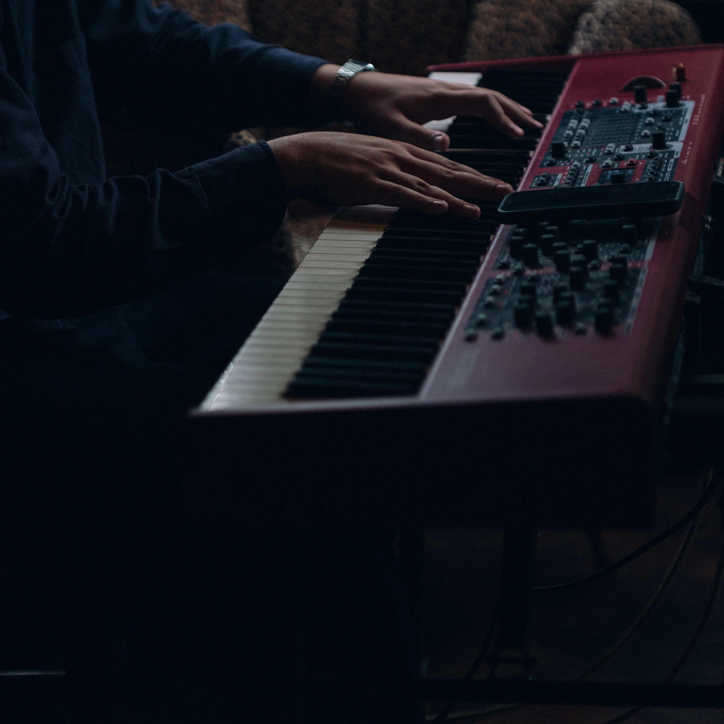 Person playing a red electronic keyboard with black and white keys in a dimly lit setting.