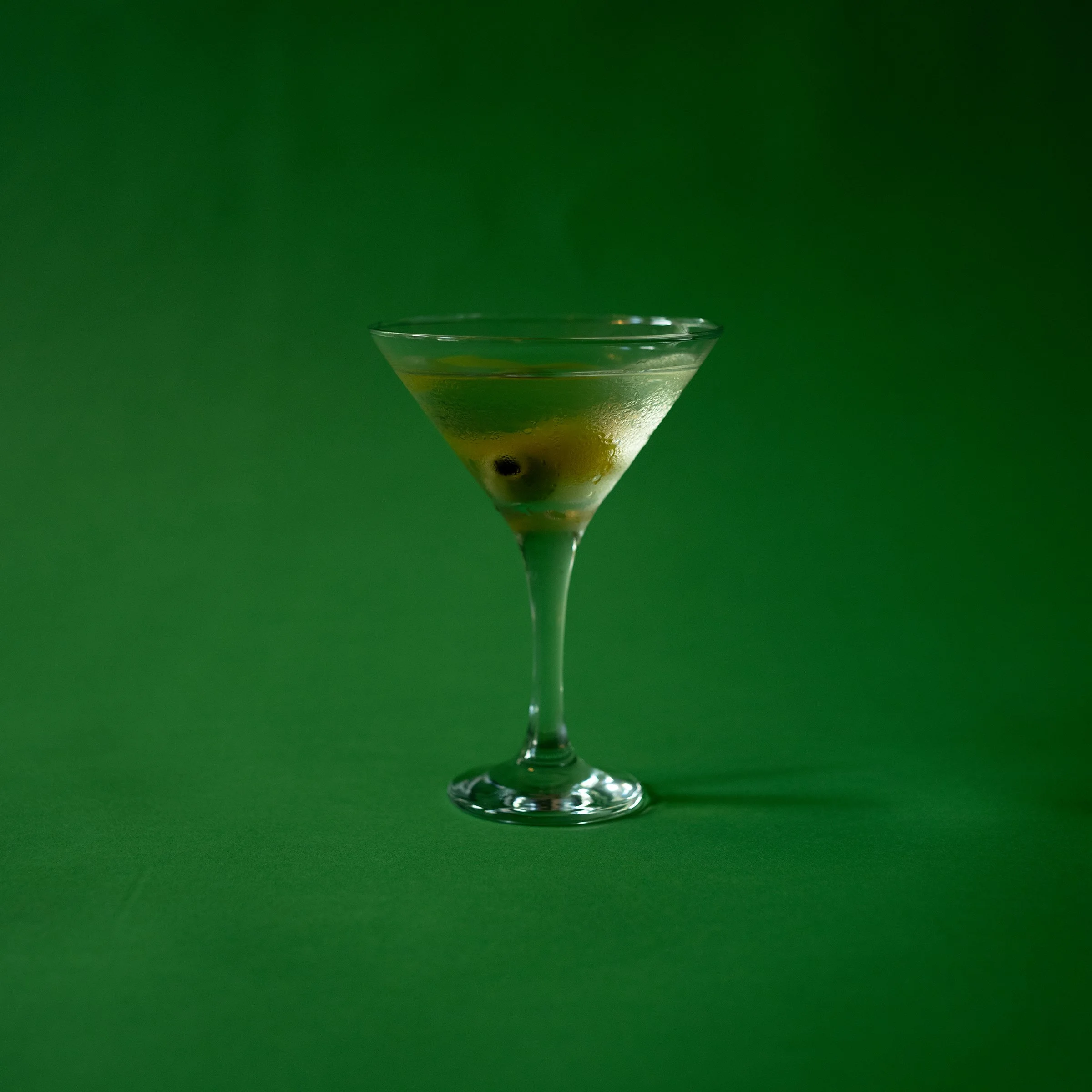 Martini glass with green olive garnish on a green background.