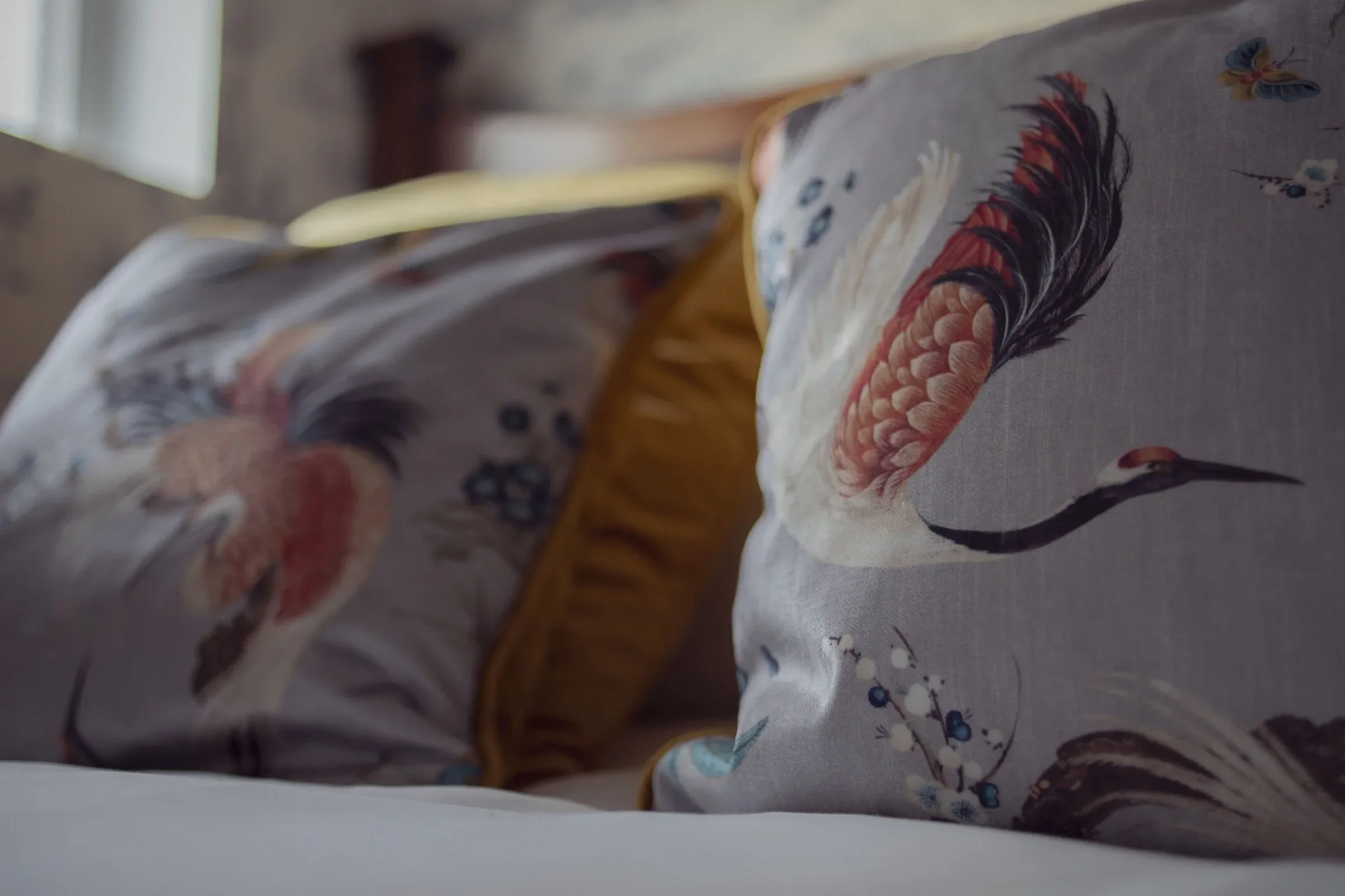 Close-up of decorative pillows with crane and nature designs on a bed in a rustic room.
