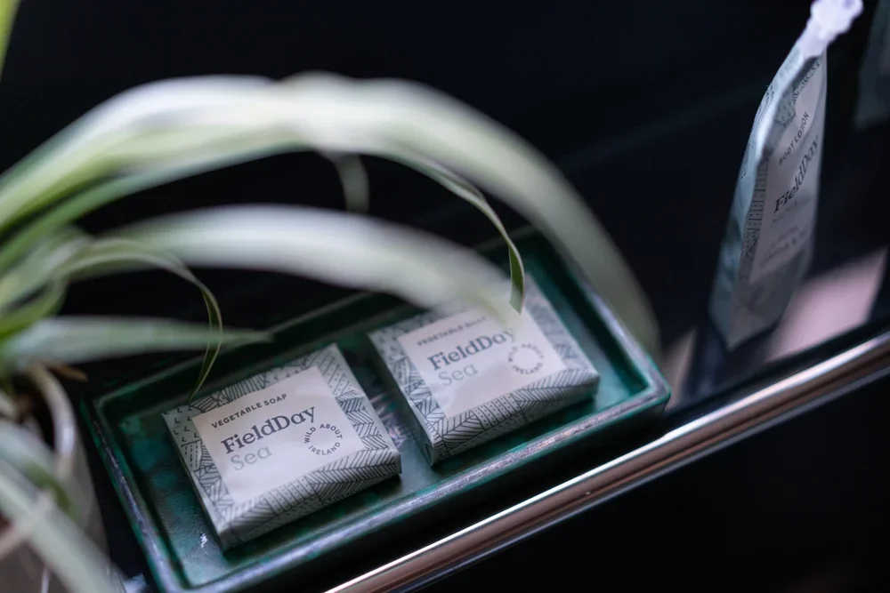 Three bars of soap labeled 'FieldDay Sea Vegetable Soap' placed in a green box, with a plant leaf partially covering the soaps, on a reflective surface.