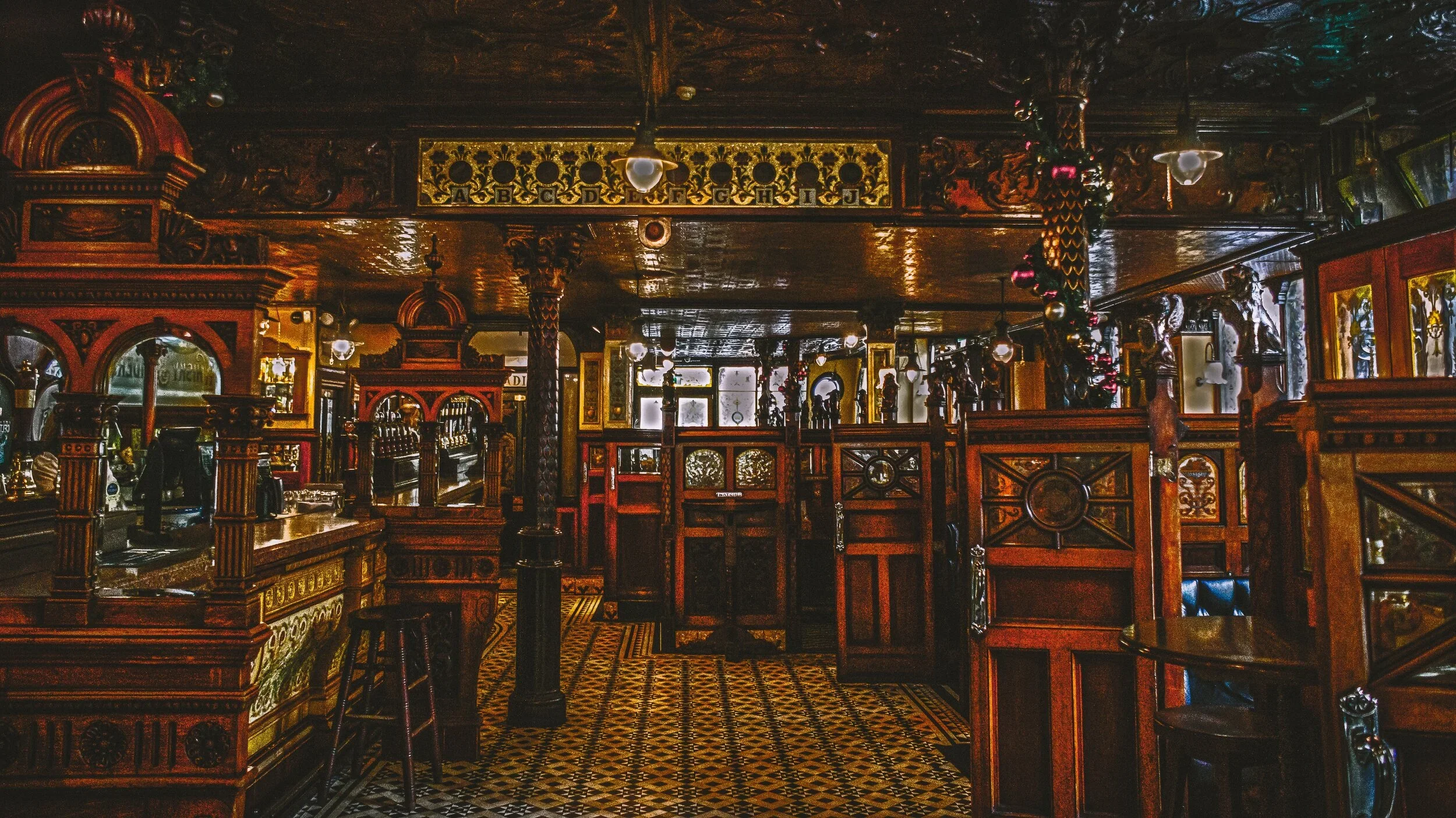 Interior of a restaurant with dark wood furnishings, ornate carvings, and colorful tile flooring, with booths and tables arranged throughout.