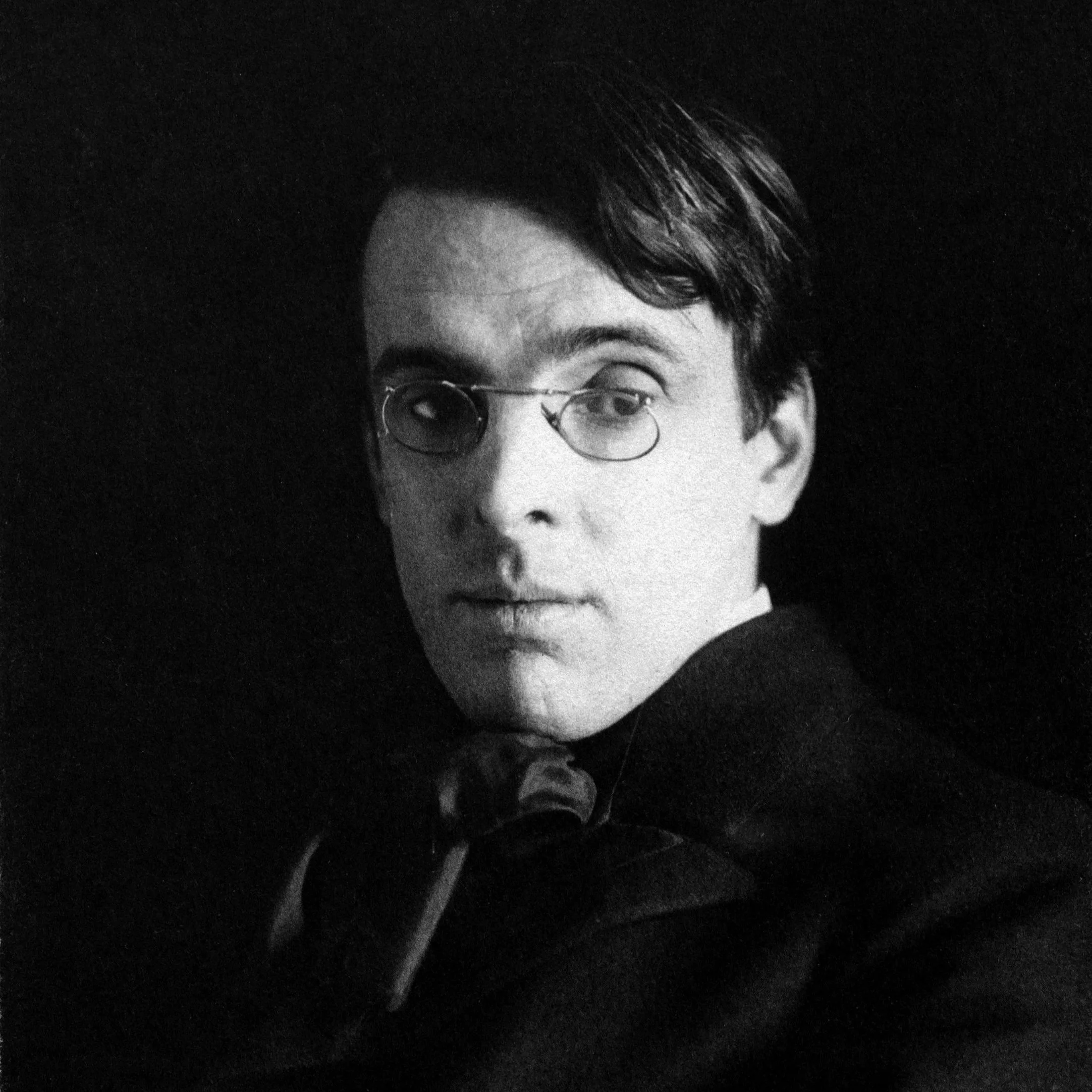 Black and white portrait of a young man with glasses, dark hair, and a serious expression, wearing a dark suit and tie.