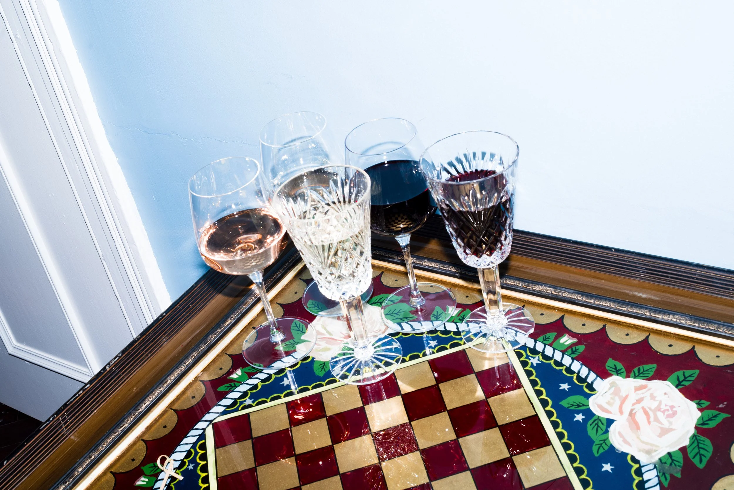 Four wine glasses on a colorful, patterned table near a white wall.